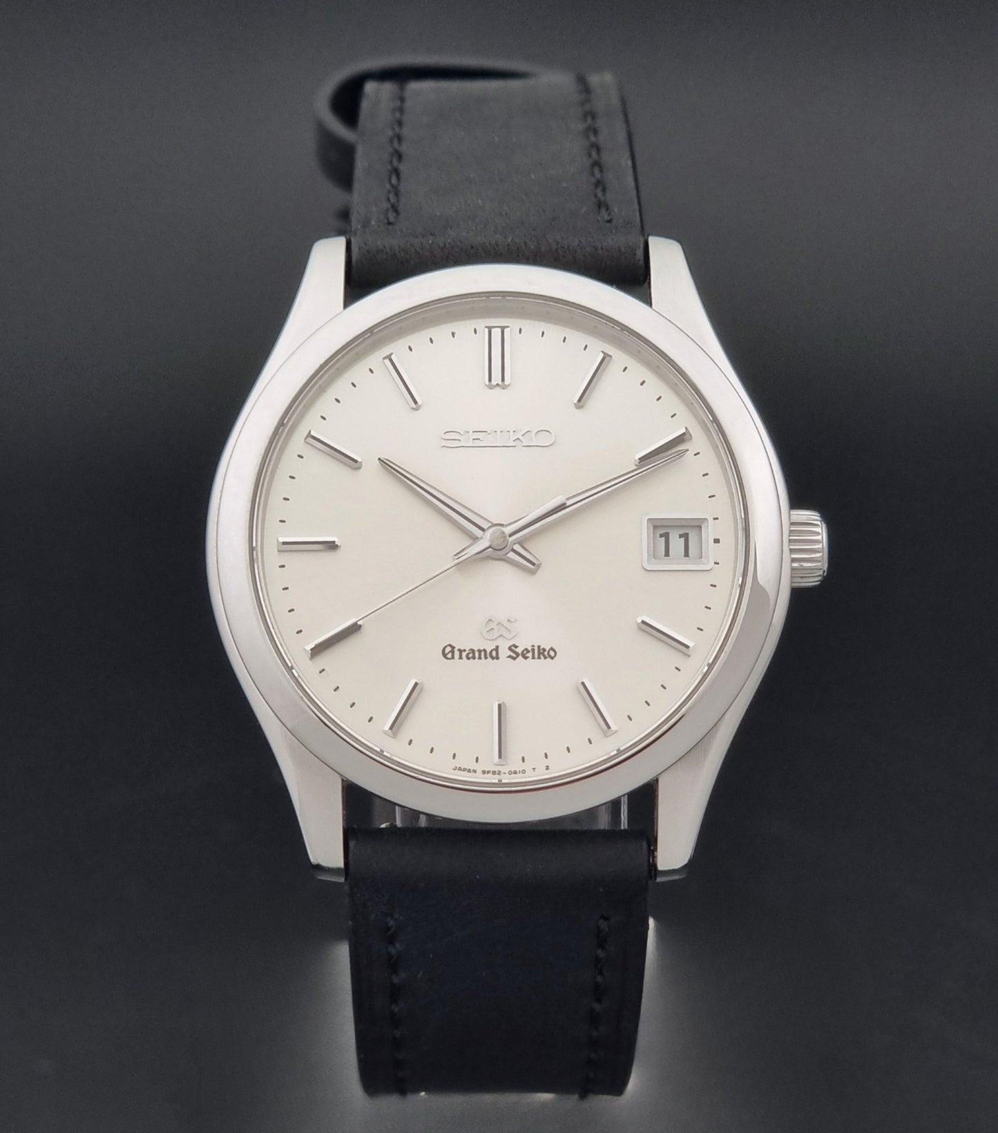 Grand Seiko SBGV001 quartz watch 9F82-0A10 with a silver-toned case,  and black leather strap, on a dark background close dial view