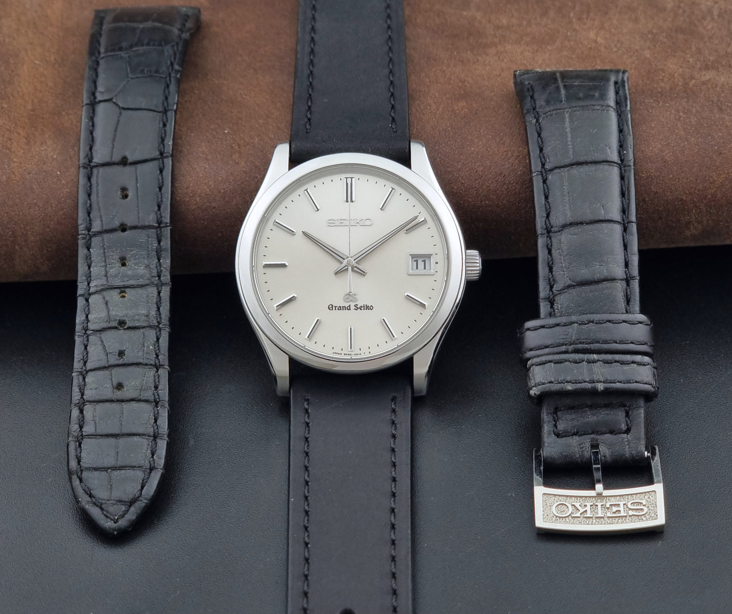 Grand Seiko SBGV001 quartz watch 9F82-0A10 with a silver-toned case,  and black leather strap, on a brown background dial view