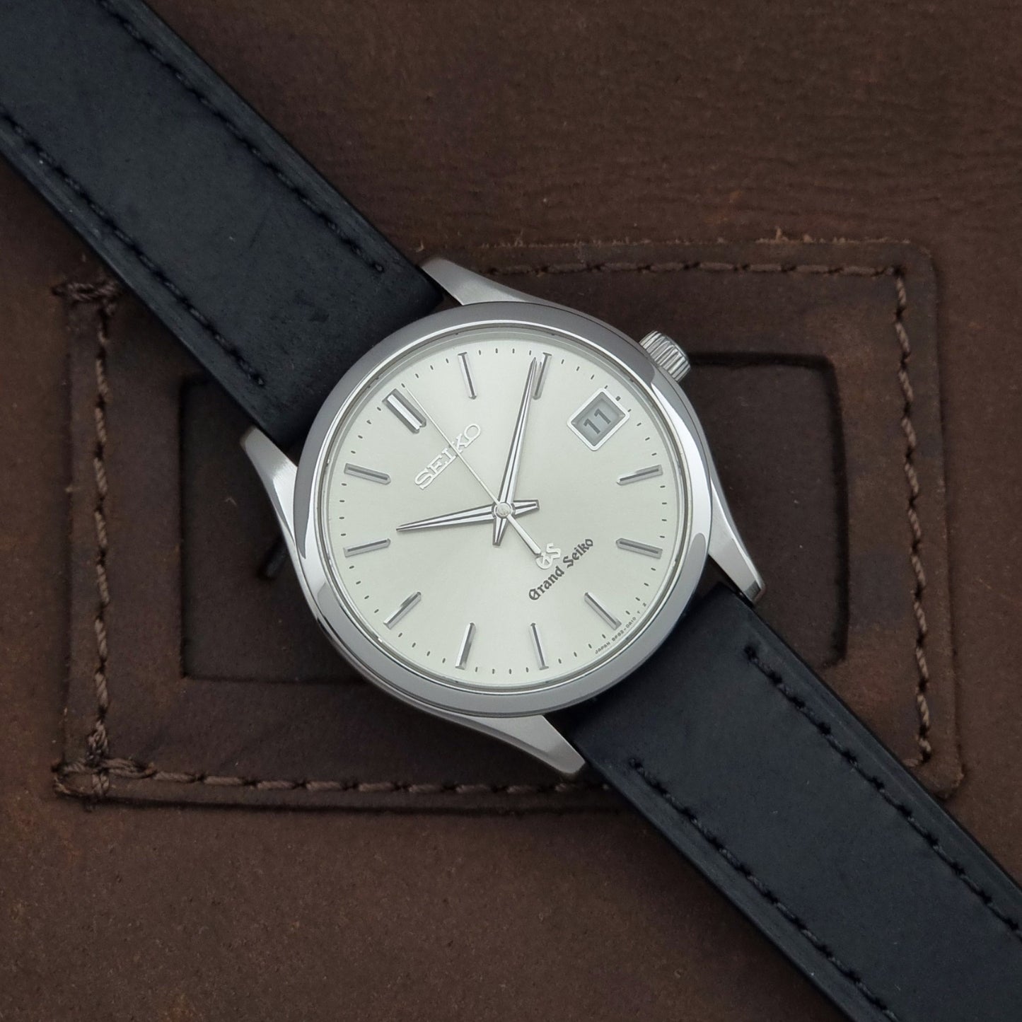 Grand Seiko SBGV001 quartz watch 9F82-0A10 with a silver-toned case,  and black leather strap, on a brown background dial