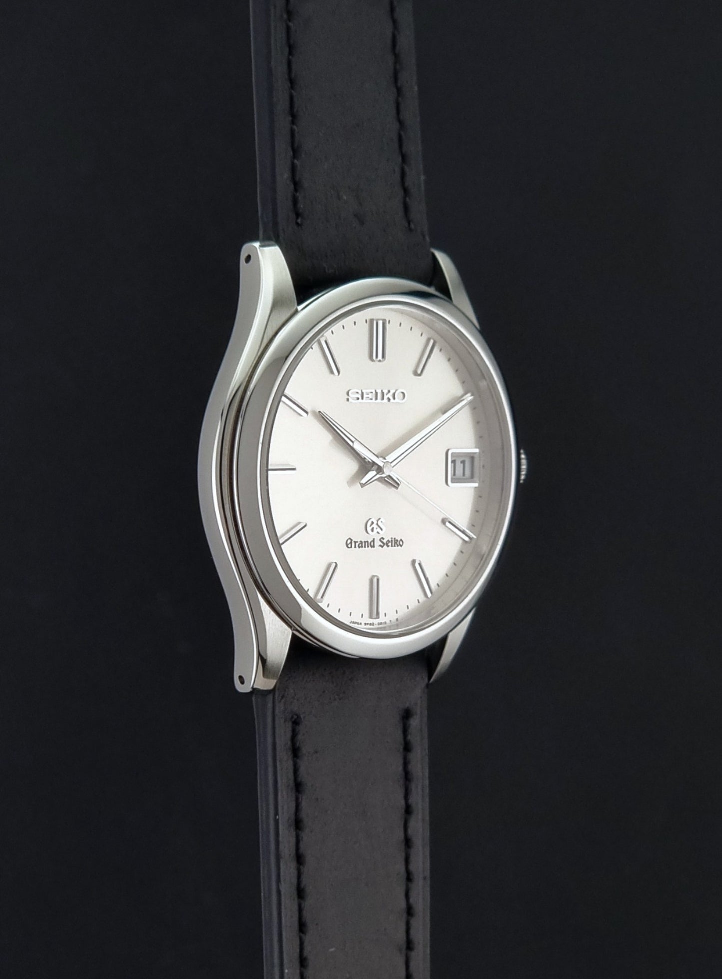 Grand Seiko SBGV001 quartz watch 9F82-0A10 with a silver-toned case,  and black leather strap, on a dark background side profile view