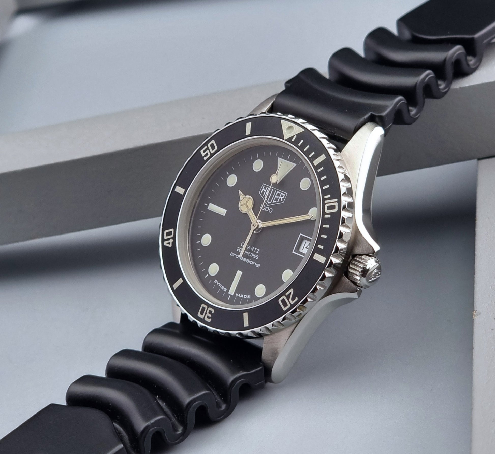 Vintage Heuer watch Professional Quartz 1000 980.013L with black strap and black dial on a light gray background crown view