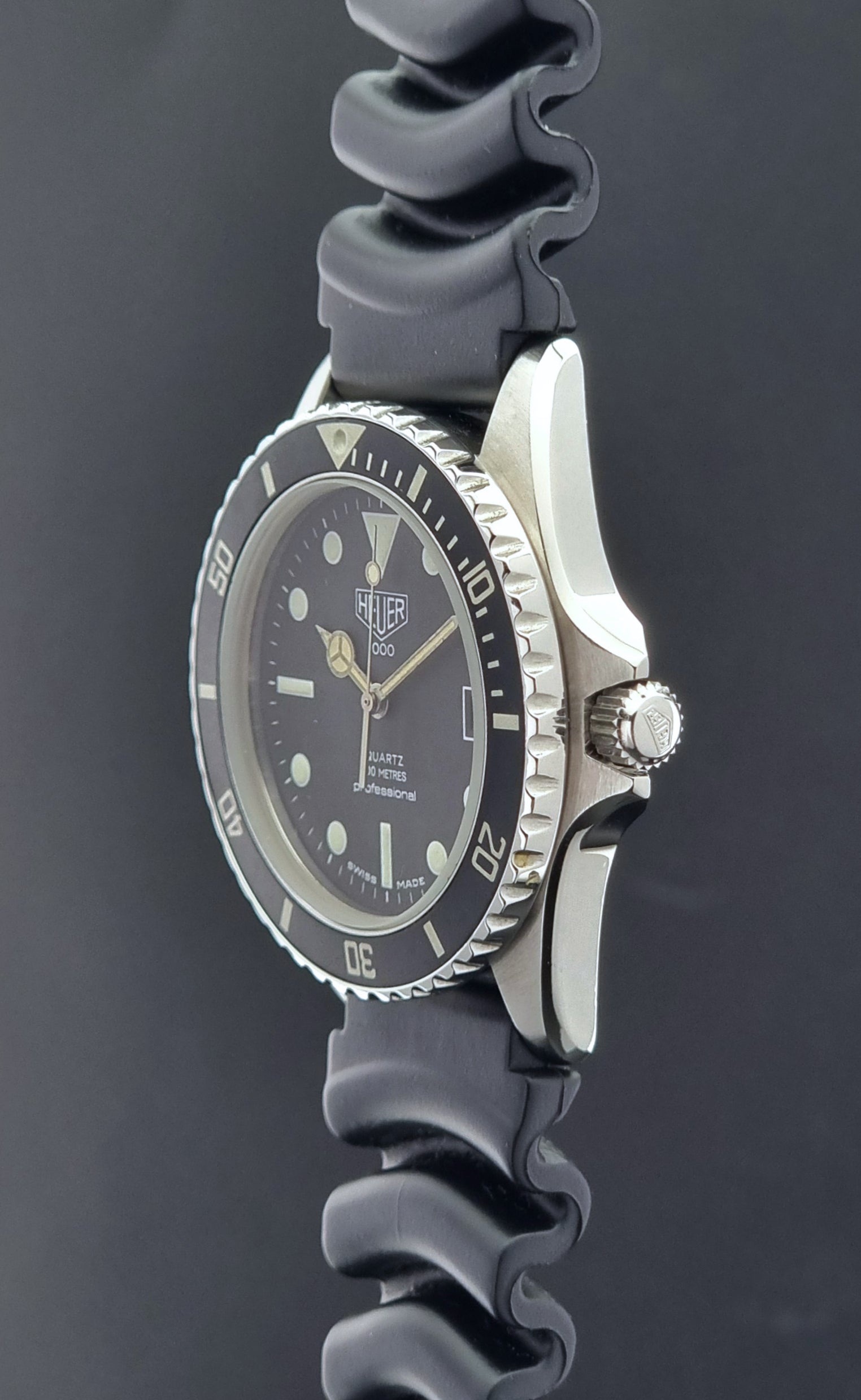 Vintage Heuer watch Professional Quartz 1000 980.013L with black strap and black dial on a light gray background crown profile view