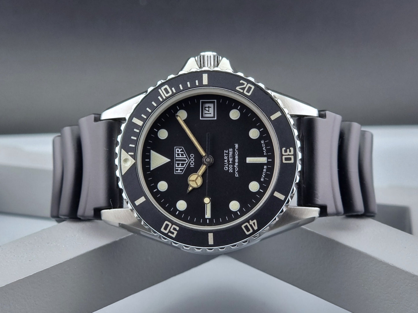 Vintage Heuer watch Professional Quartz 1000 980.013L with black strap and black dial on a light gray background close front view