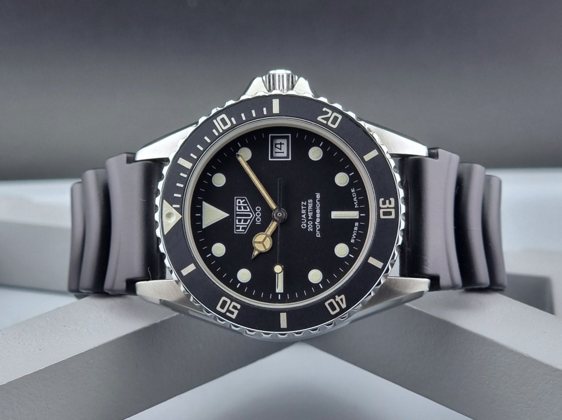 Vintage Heuer watch Professional Quartz 1000 980.013L with black strap and black dial on a light gray background close front view