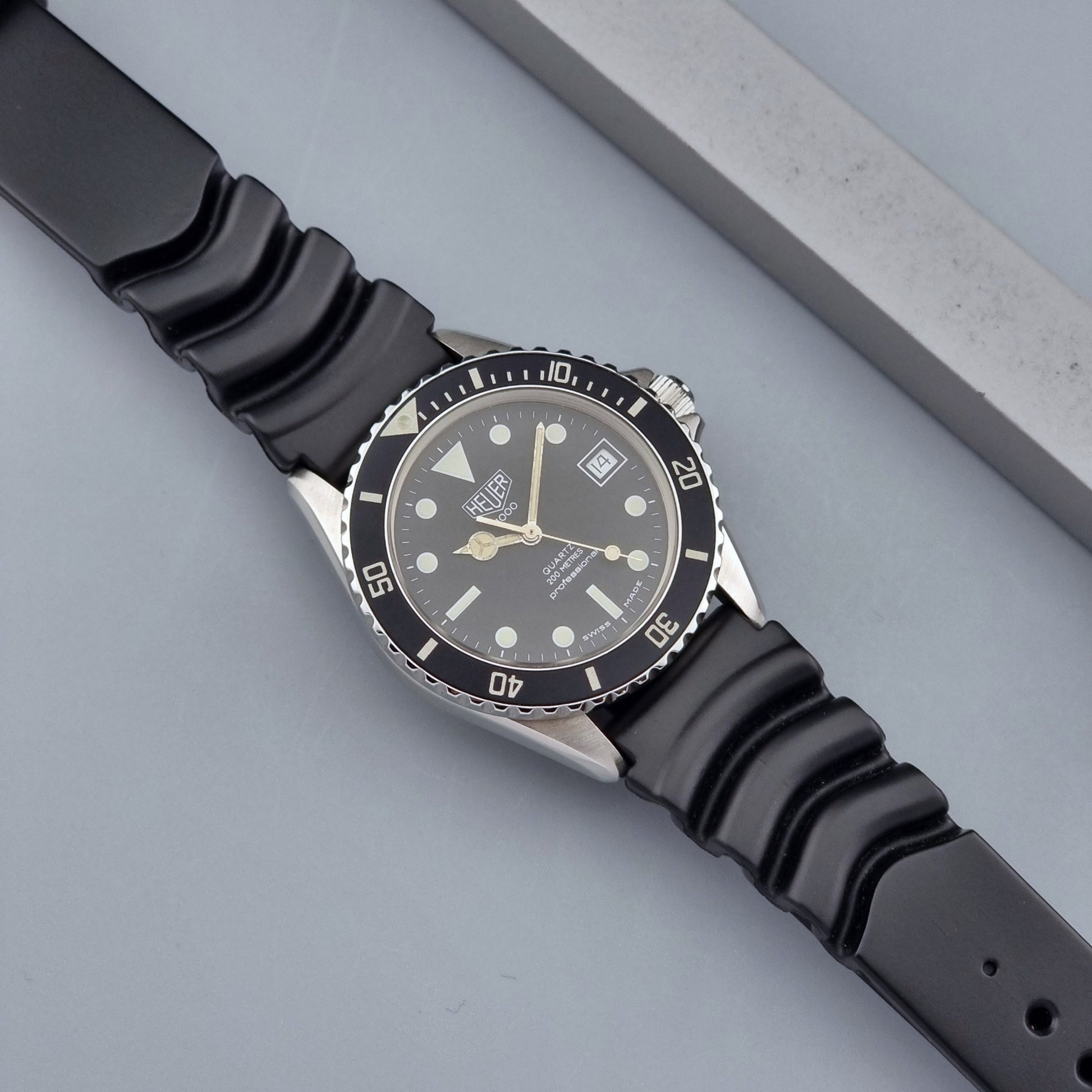 Vintage Heuer watch Professional Quartz 1000 980.013L with black strap and black dial on a light gray background close up dial view