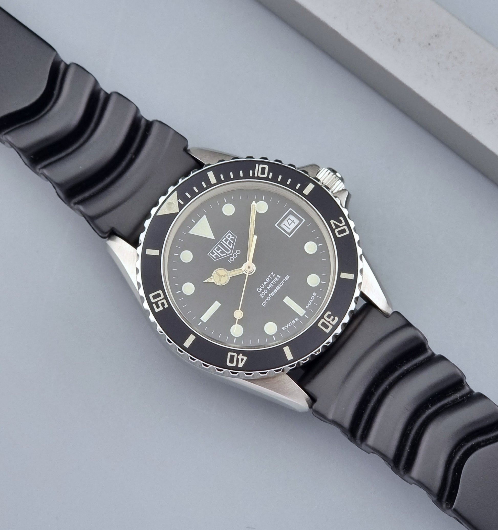 Vintage Heuer watch Professional Quartz 1000 980.013L with black strap and black dial on a light gray background dial