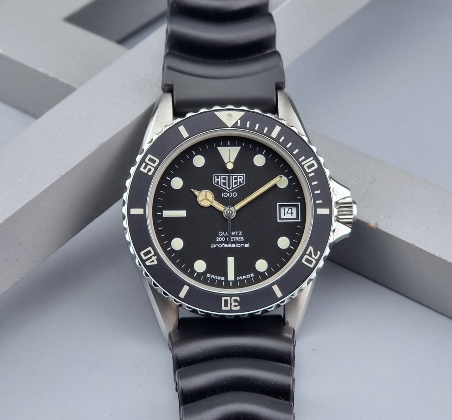 Vintage Heuer watch Professional Quartz 1000 980.013L with black strap and black dial on a light gray background front view