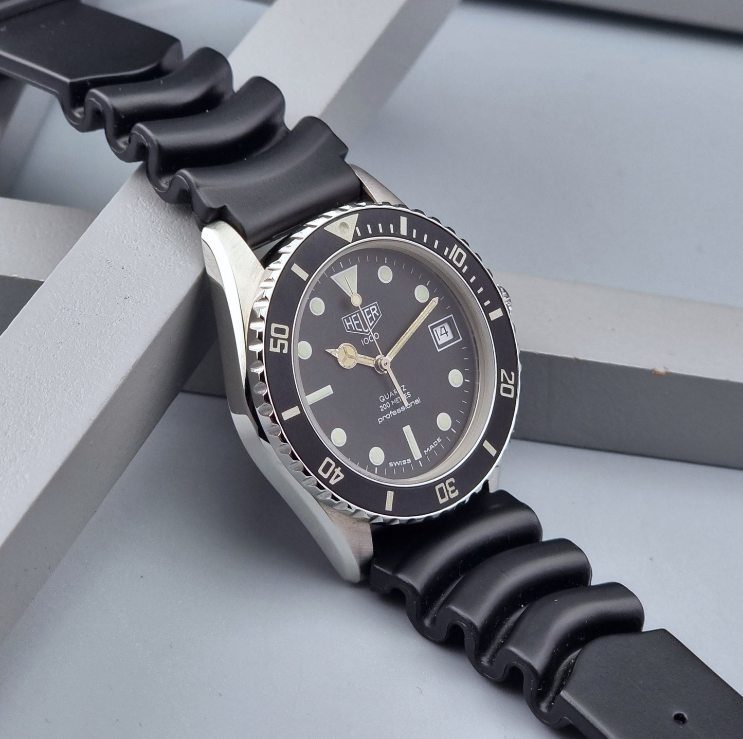 Vintage Heuer watch Professional Quartz 1000 980.013L with black strap and black dial on a light gray background side view