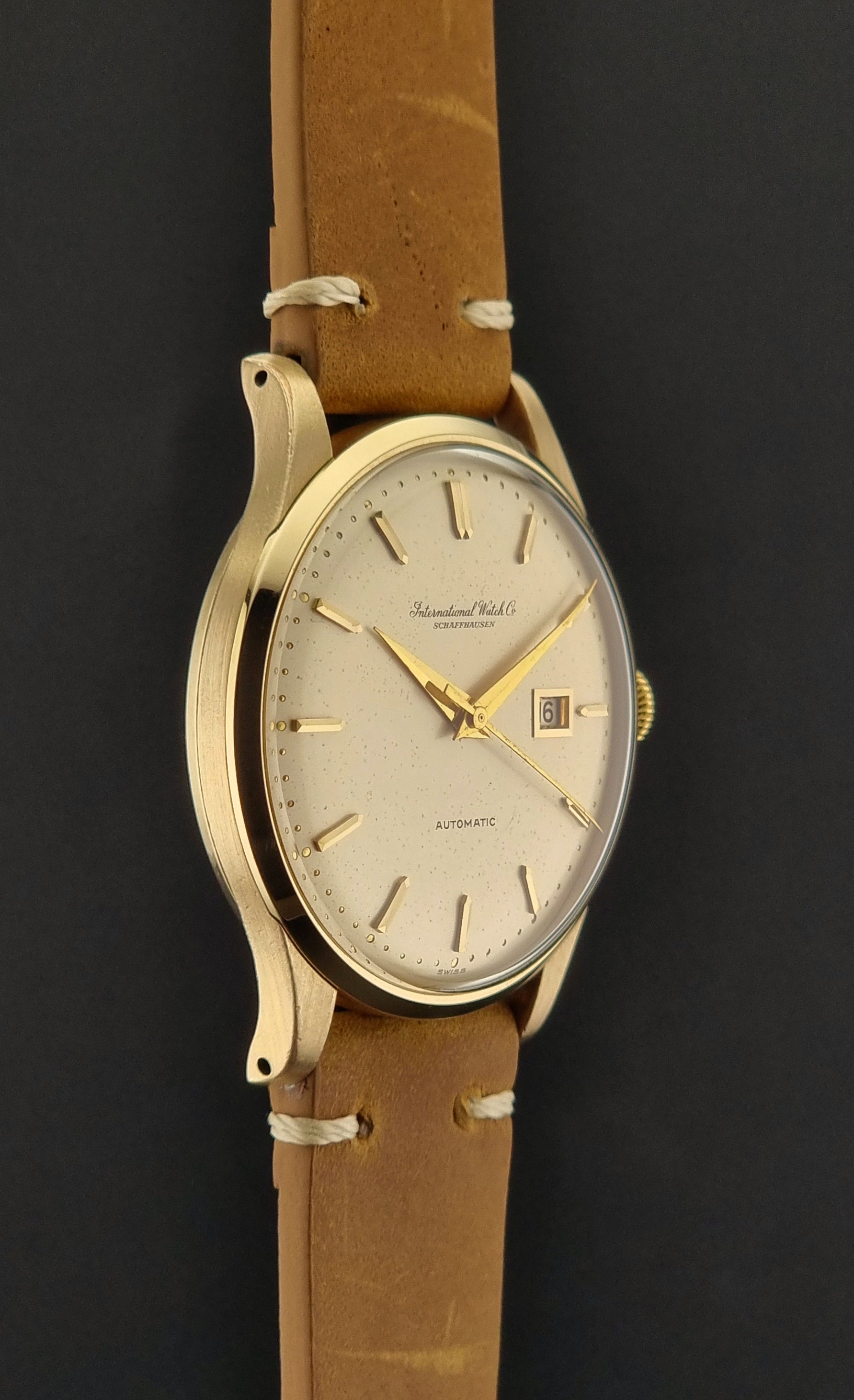 A vintage gold-plated IWC watch with a champagne dial, manual winding, and a brown leather strap