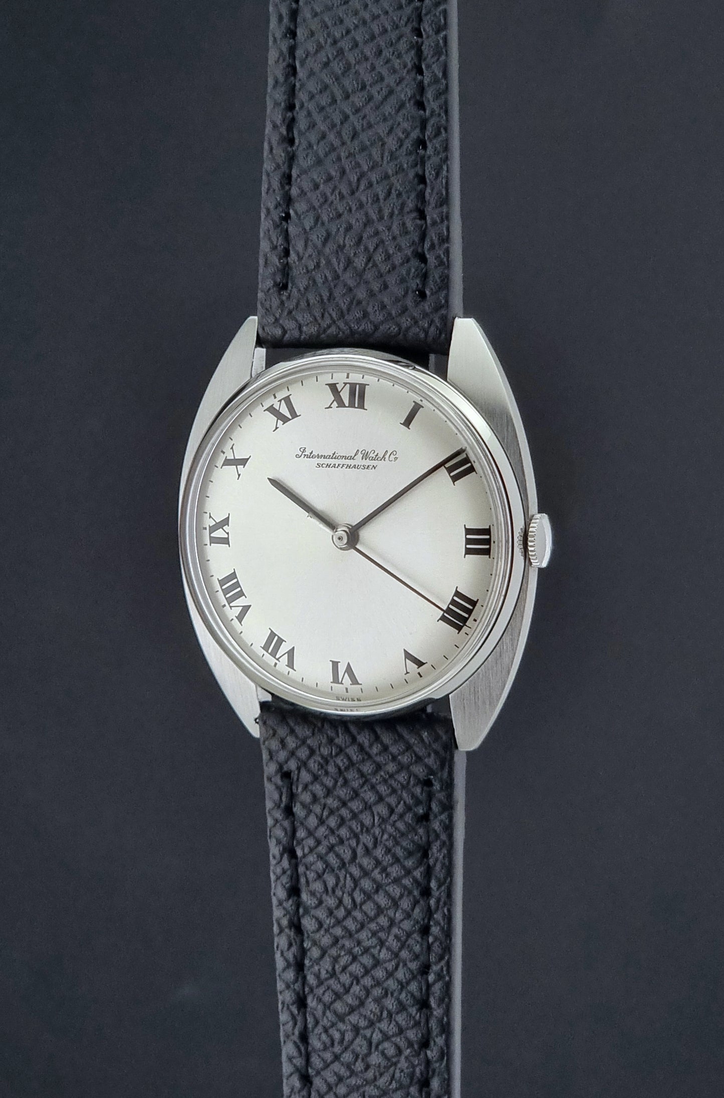 Vintage IWC R1419 Wristwatch with a black strap and silver dial on a dark background crown profile view