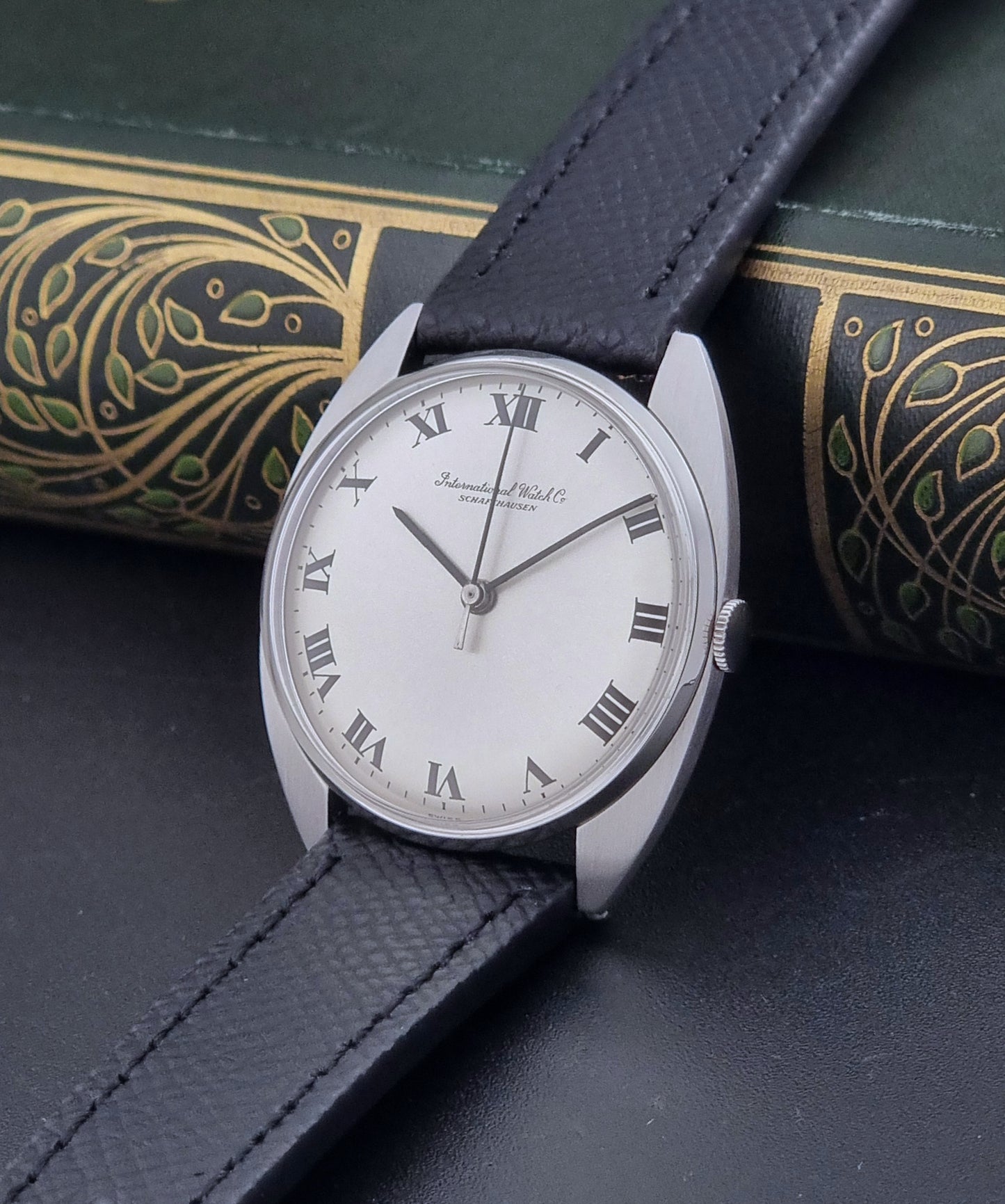 Vintage IWC R1419 Wristwatch with a black strap and silver dial on a dark background crown view