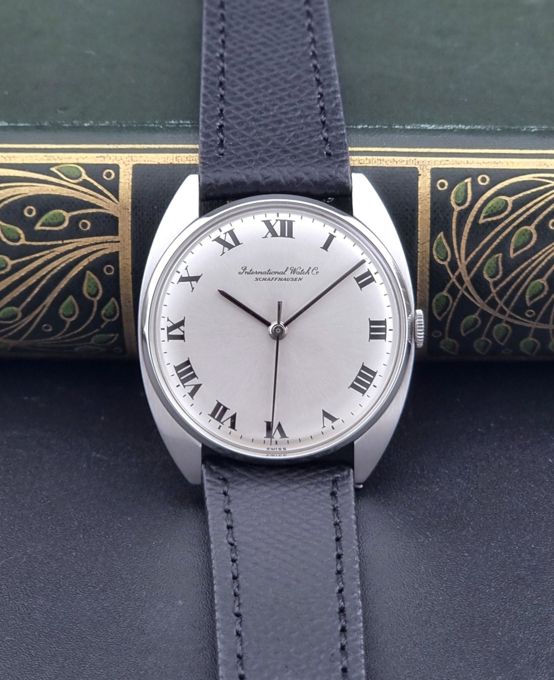 Vintage IWC R1419 Wristwatch with a black strap and silver dial on a dark background front view