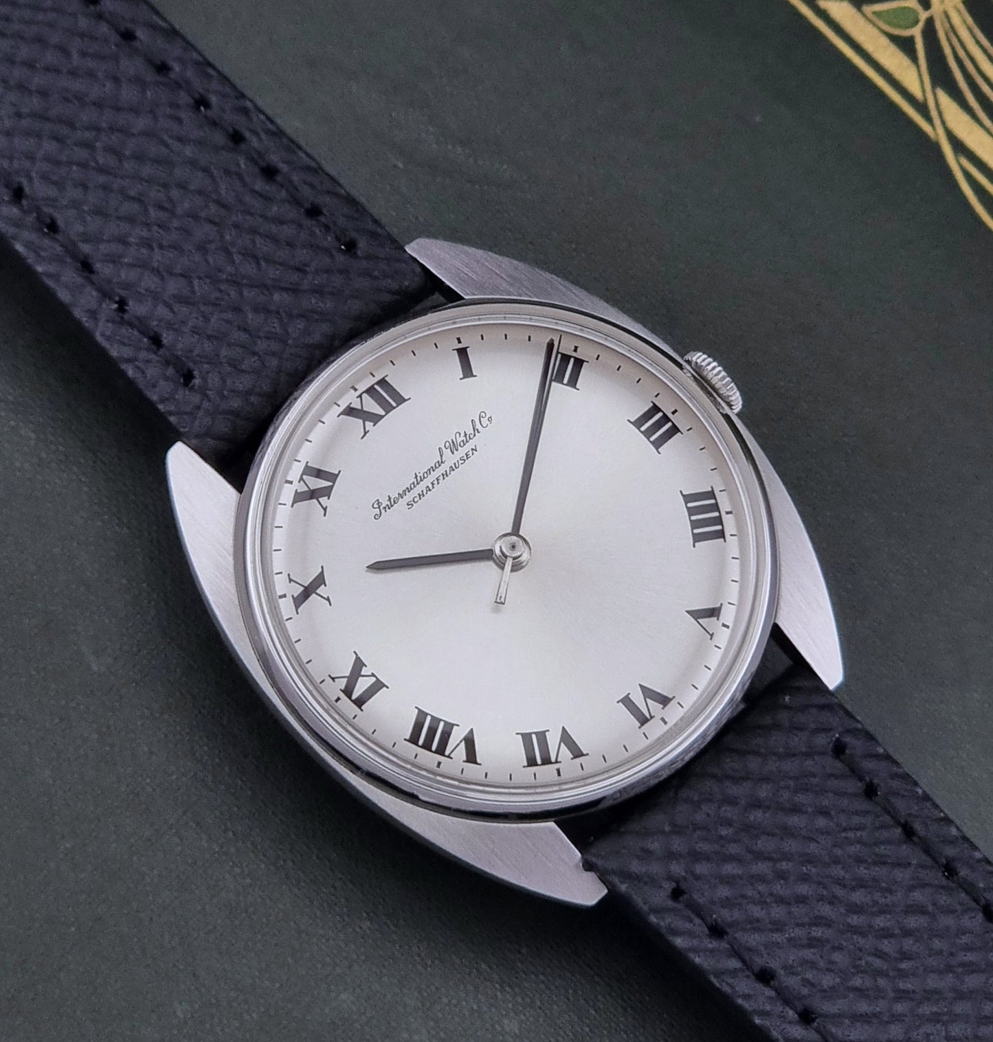 Vintage IWC R1419 Wristwatch with a black strap and silver dial on a dark background close up dial view