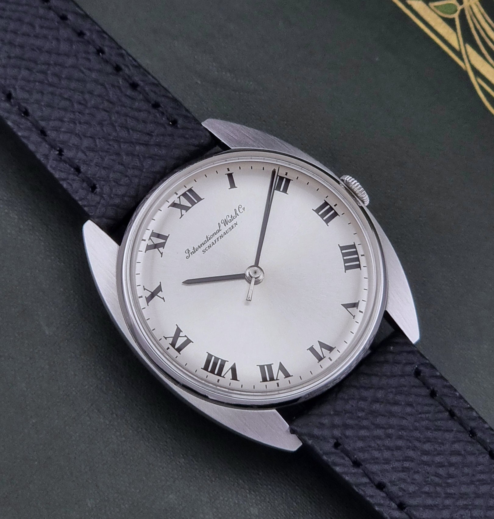 Vintage IWC R1419 Wristwatch with a black strap and silver dial on a dark background close up dial view