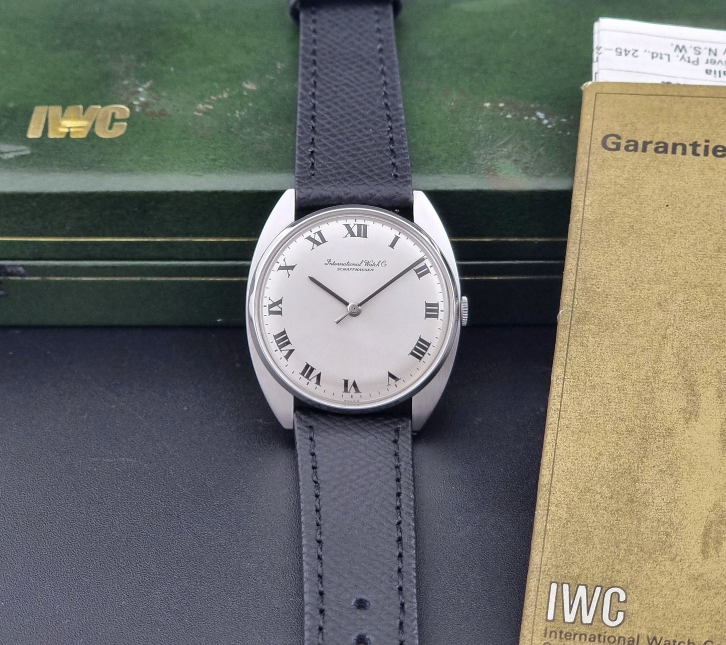 Vintage IWC R1419 Wristwatch with a black strap and silver dial on a dark background dial and papers view
