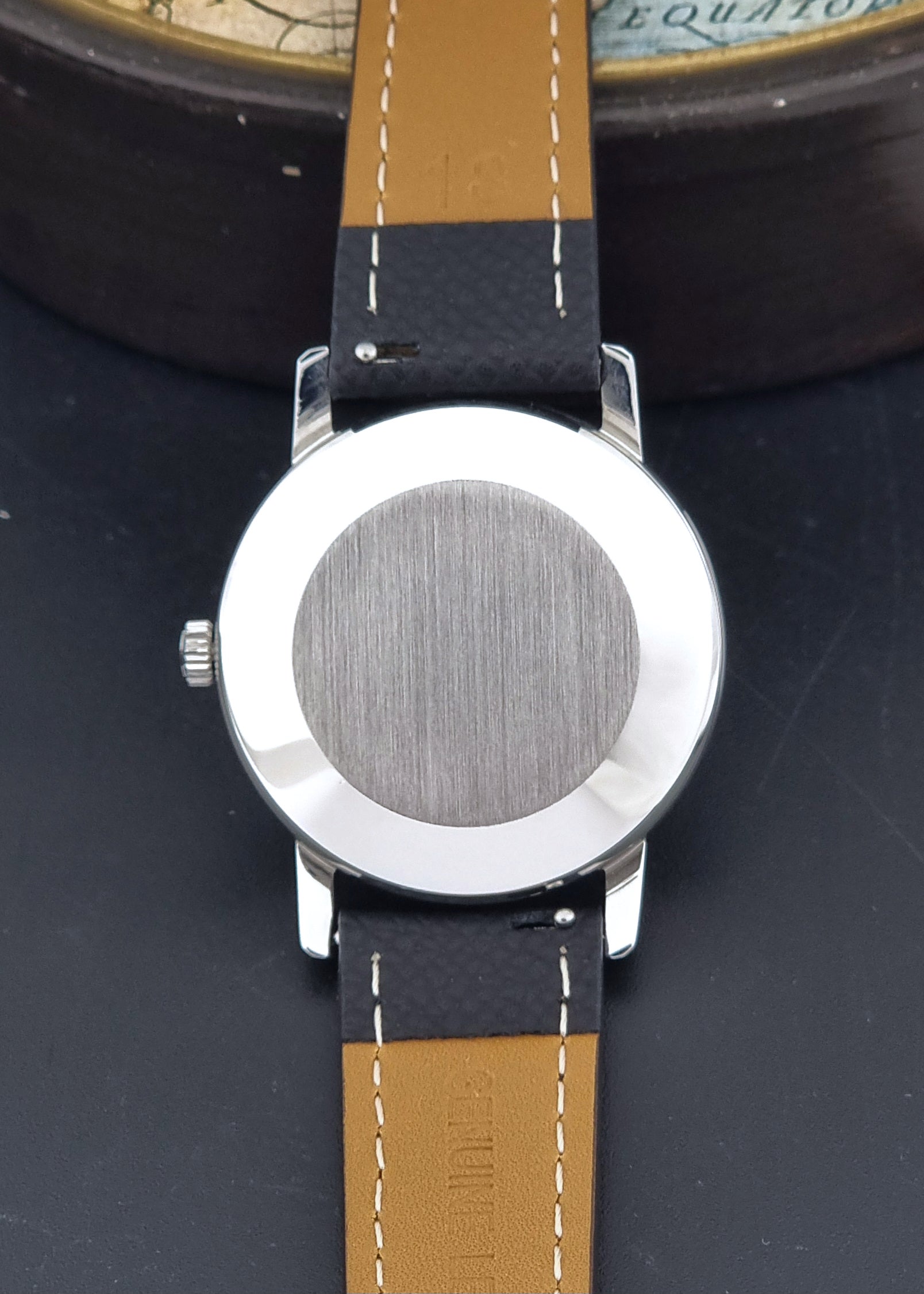 Vintage IWC R802A watch with a silver-toned case,  and textured black leather strap, on a dark background back view