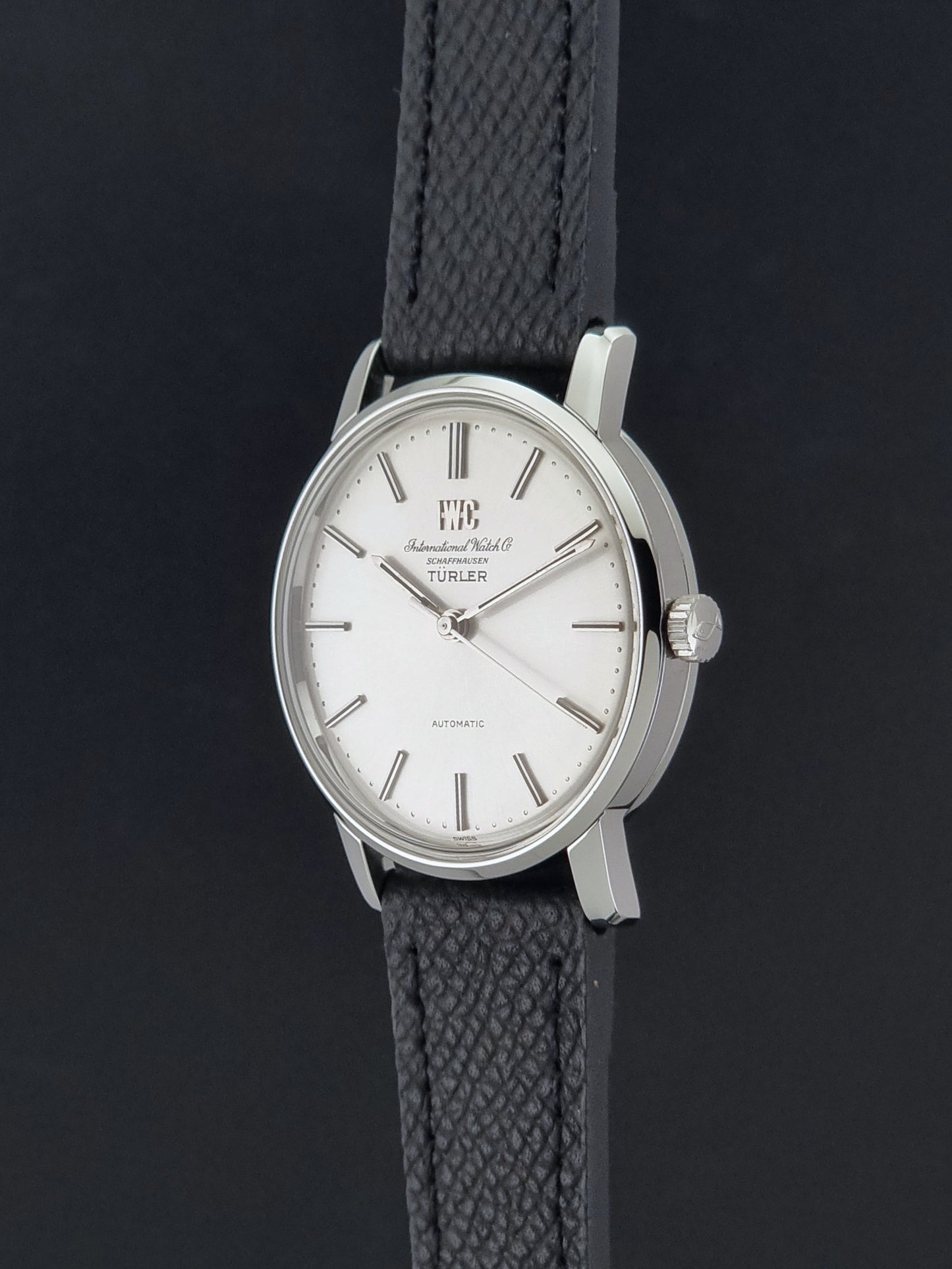 Vintage IWC R802A watch with a silver-toned case,  and textured black leather strap, on a dark background crown profile view