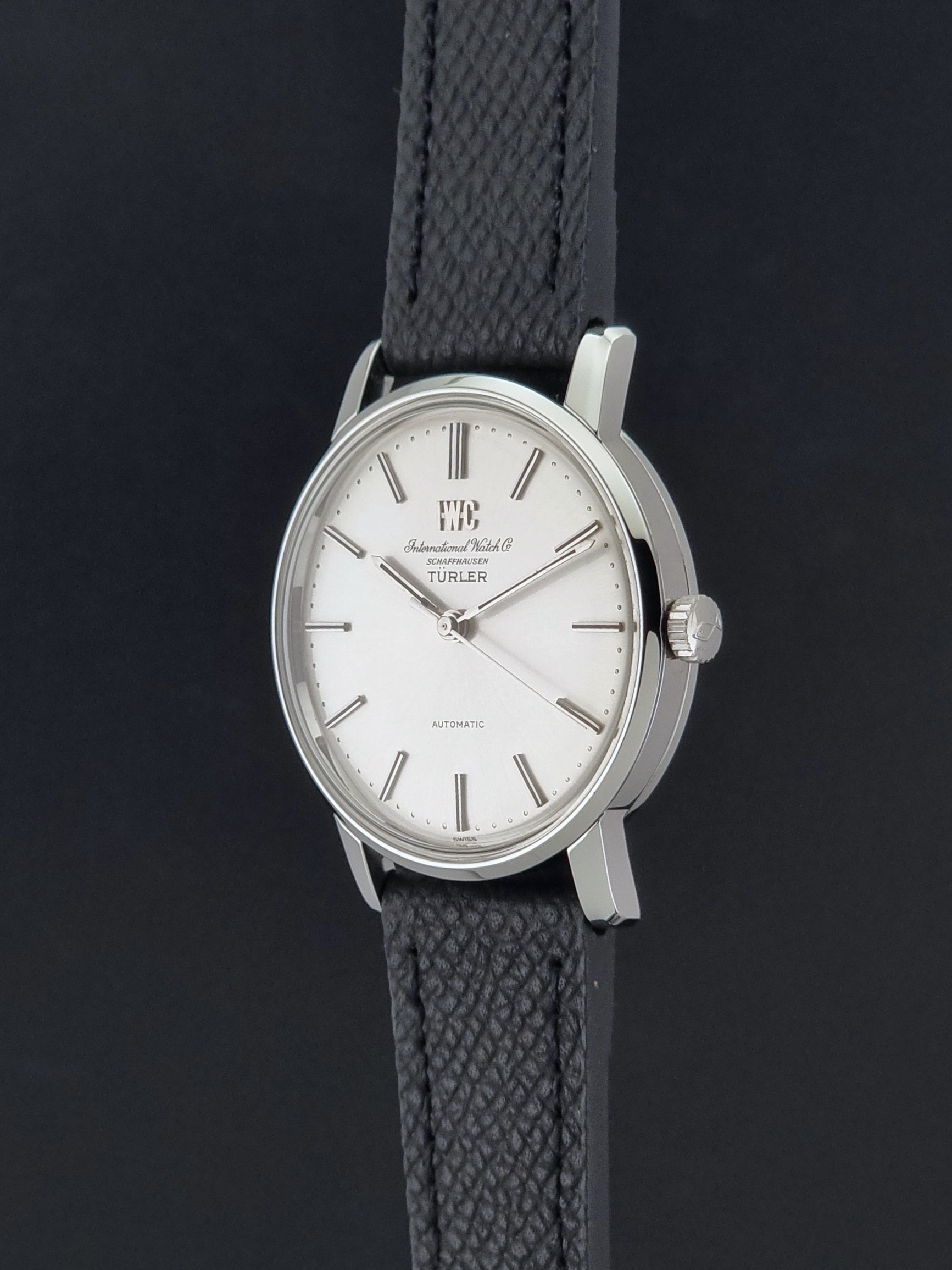 Vintage IWC R802A watch with a silver-toned case,  and textured black leather strap, on a dark background crown profile view
