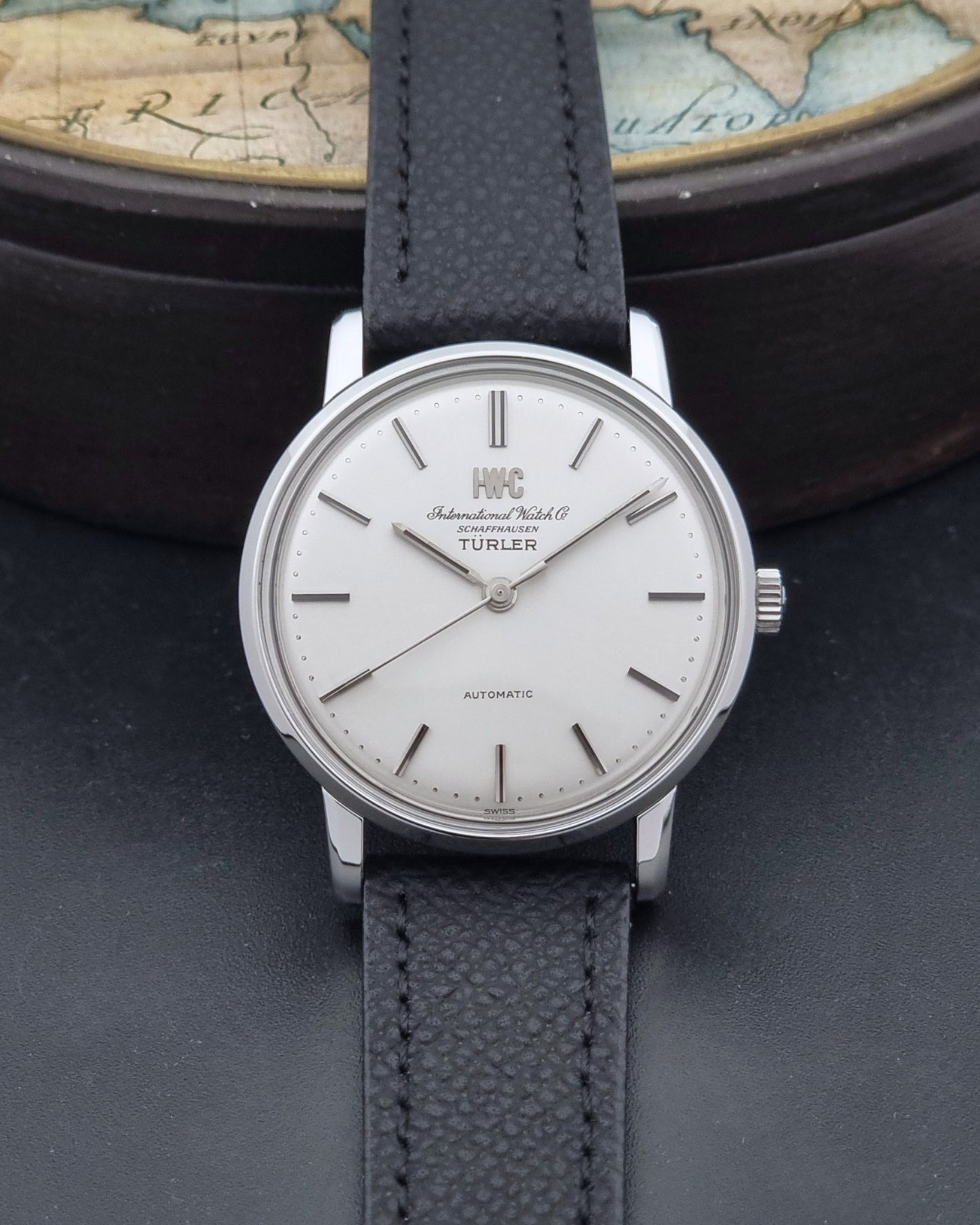Vintage IWC R802A watch with a silver-toned case,  and textured black leather strap, on a dark background dial view