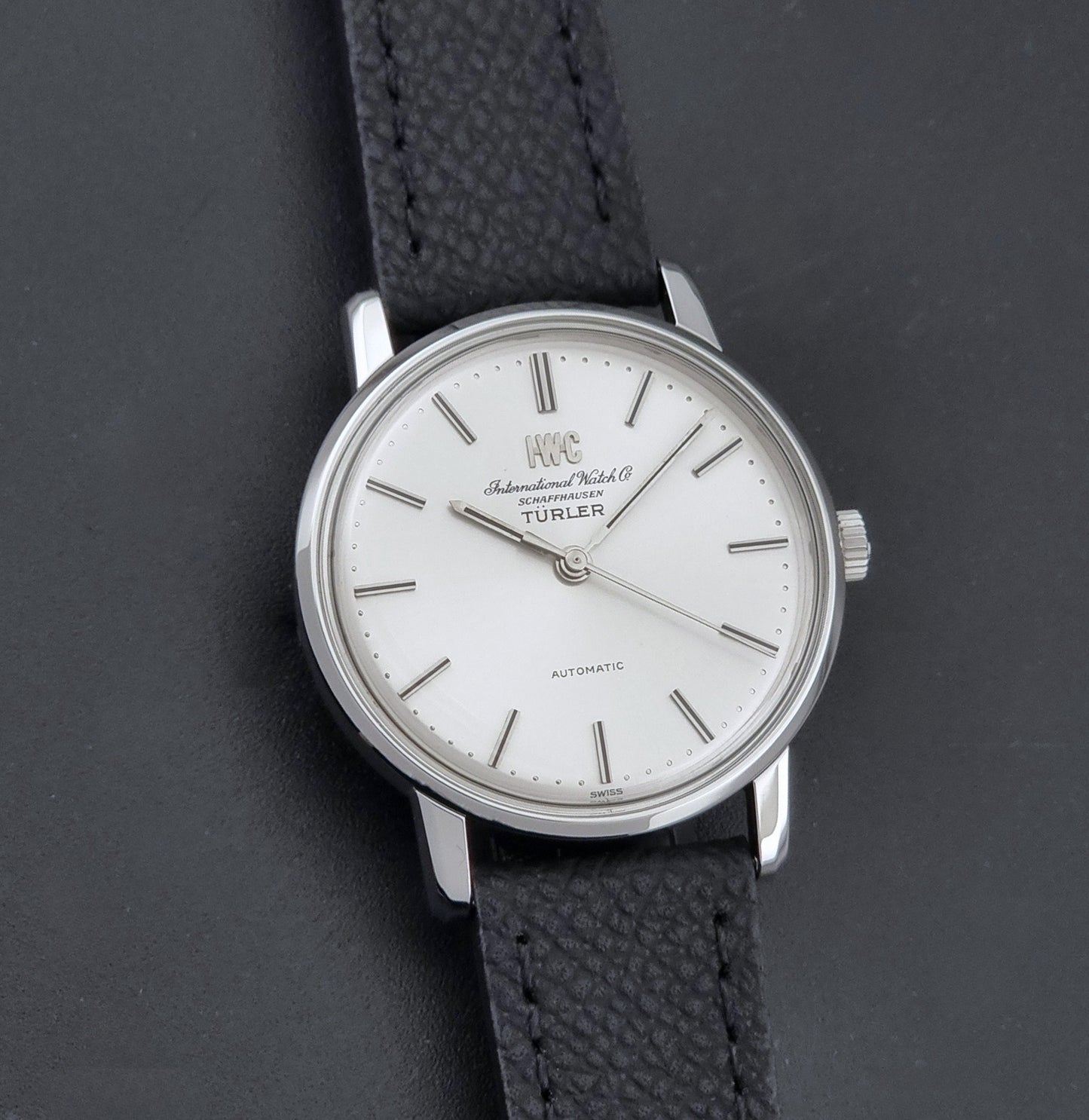 Vintage IWC R802A watch with a silver-toned case,  and textured black leather strap, on a dark background front view