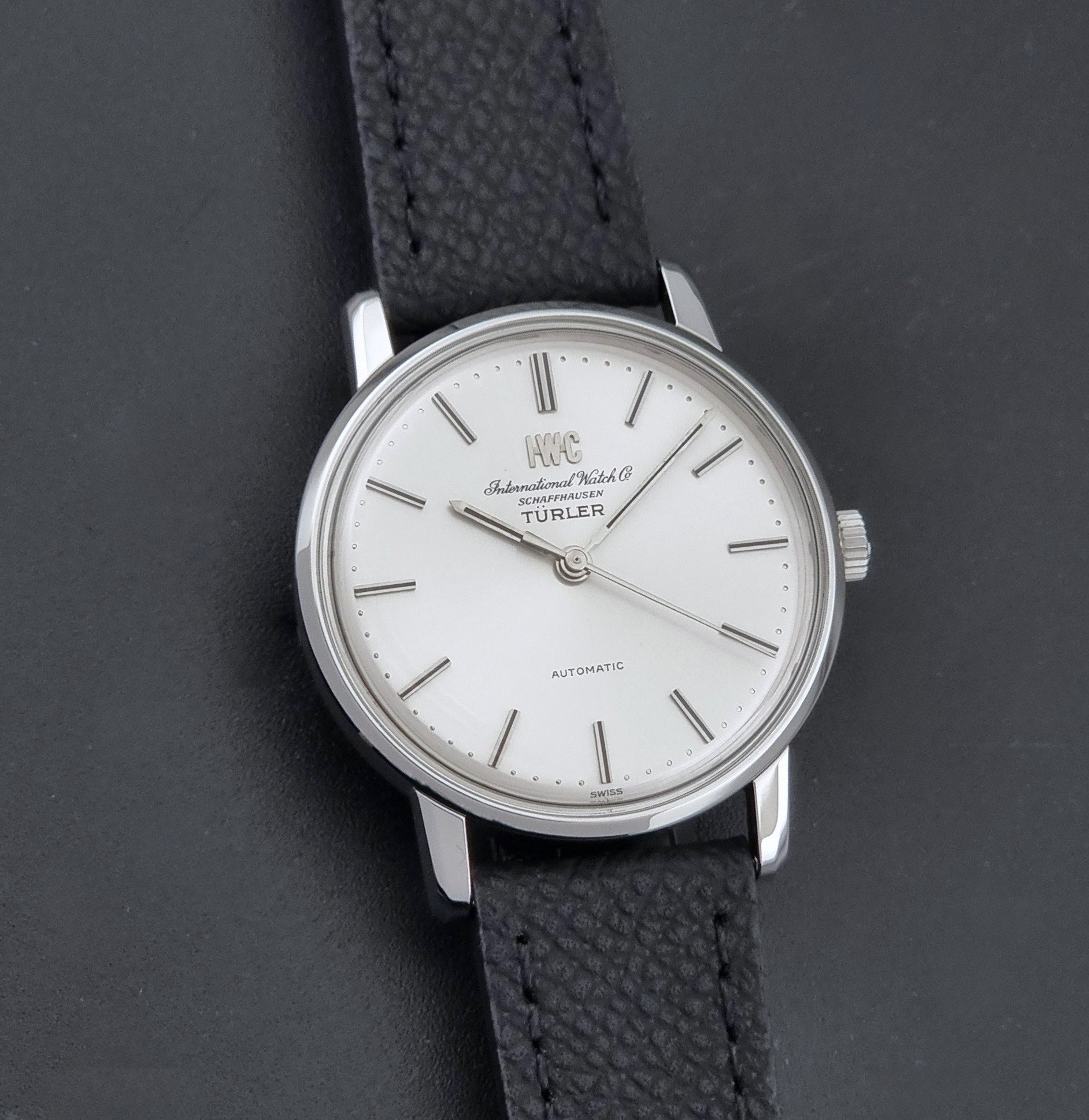Vintage IWC R802A watch with a silver-toned case,  and textured black leather strap, on a dark background front view