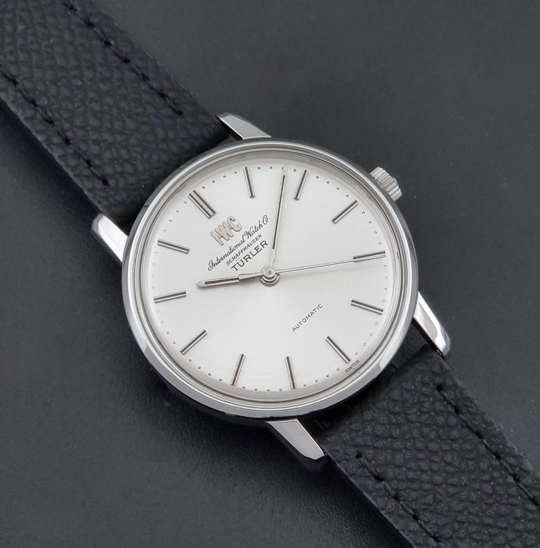 Vintage IWC R802A watch with a silver-toned case,  and textured black leather strap, on a dark background close up dial view