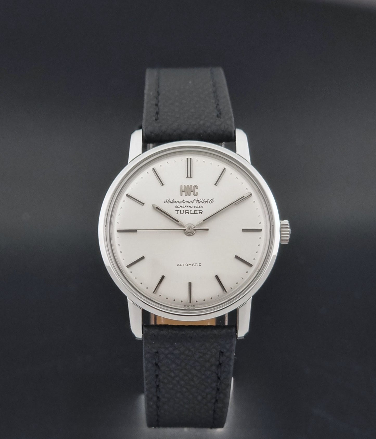 Vintage IWC R802A watch with a silver-toned case,  and textured black leather strap, on a dark background close dial view