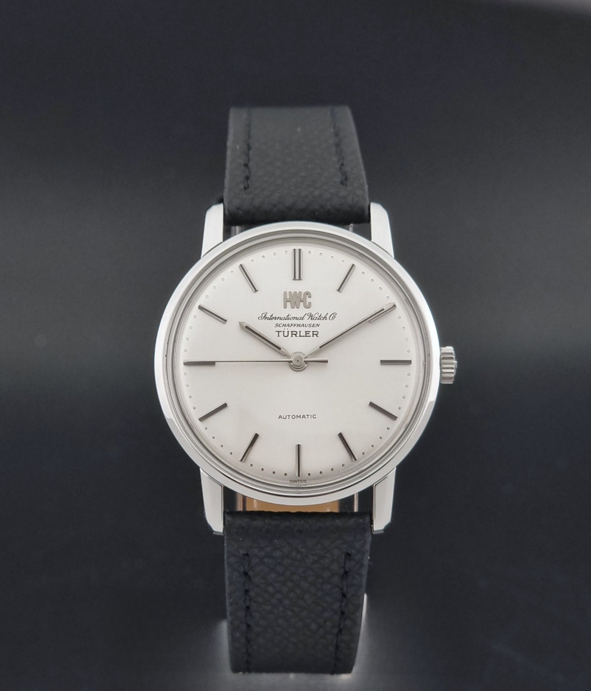 Vintage IWC R802A watch with a silver-toned case,  and textured black leather strap, on a dark background close dial view