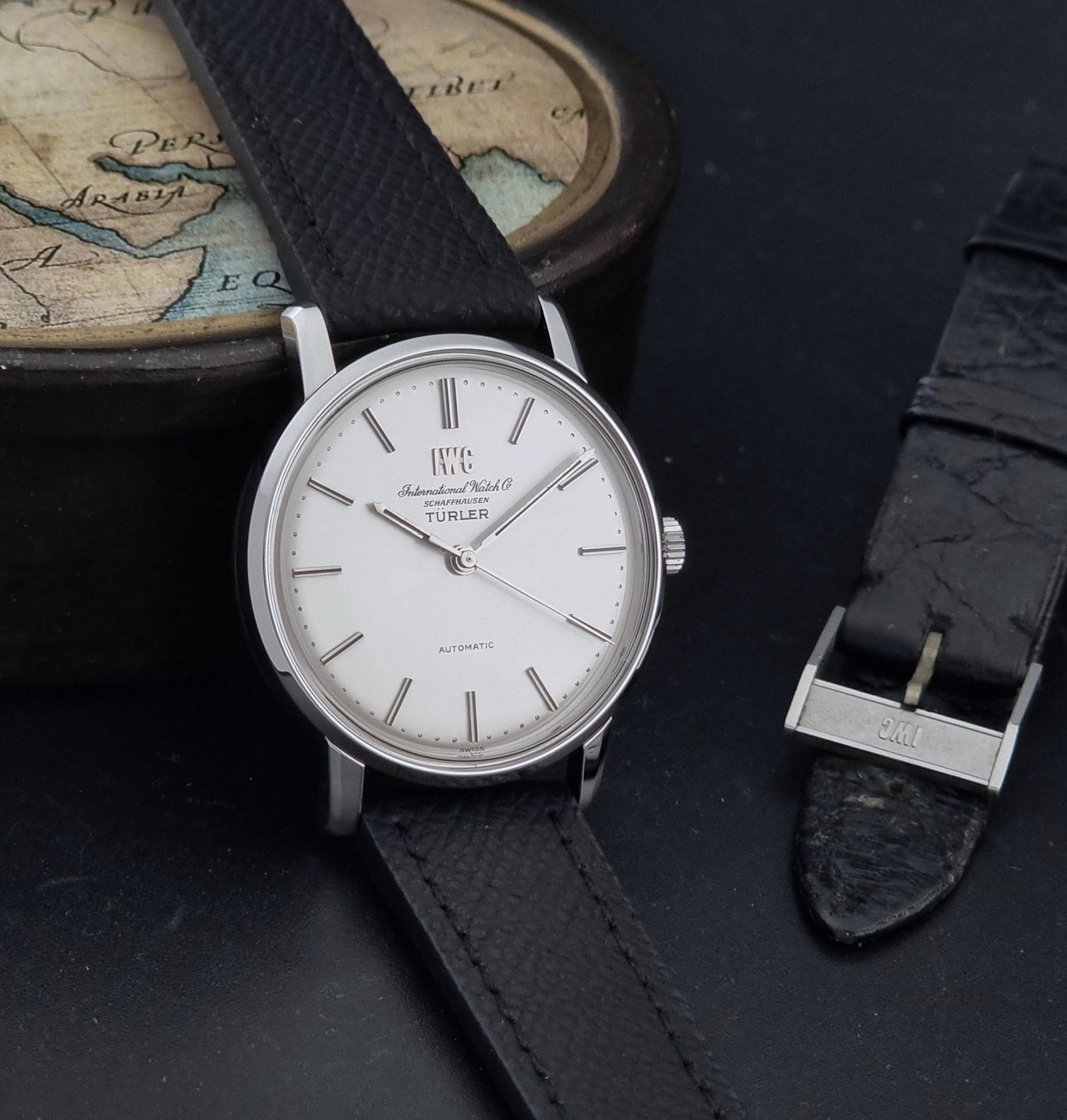 Vintage IWC R802A watch with a silver-toned case,  and textured black leather strap, on a dark background side view