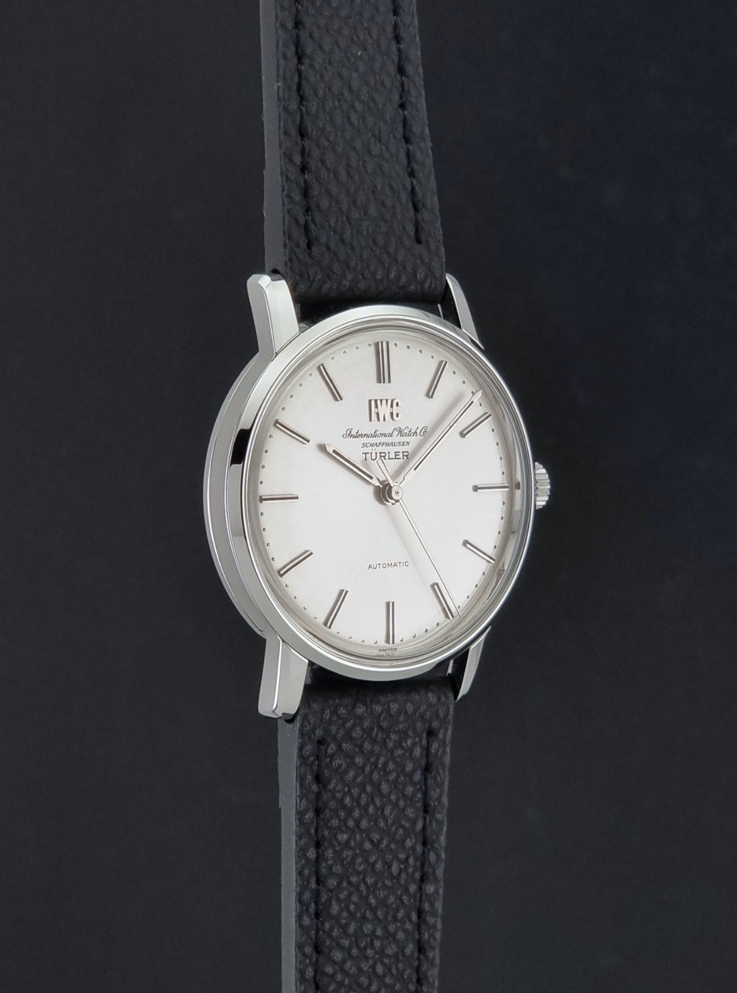 Vintage IWC R802A watch with a silver-toned case,  and textured black leather strap, on a dark background side profile view