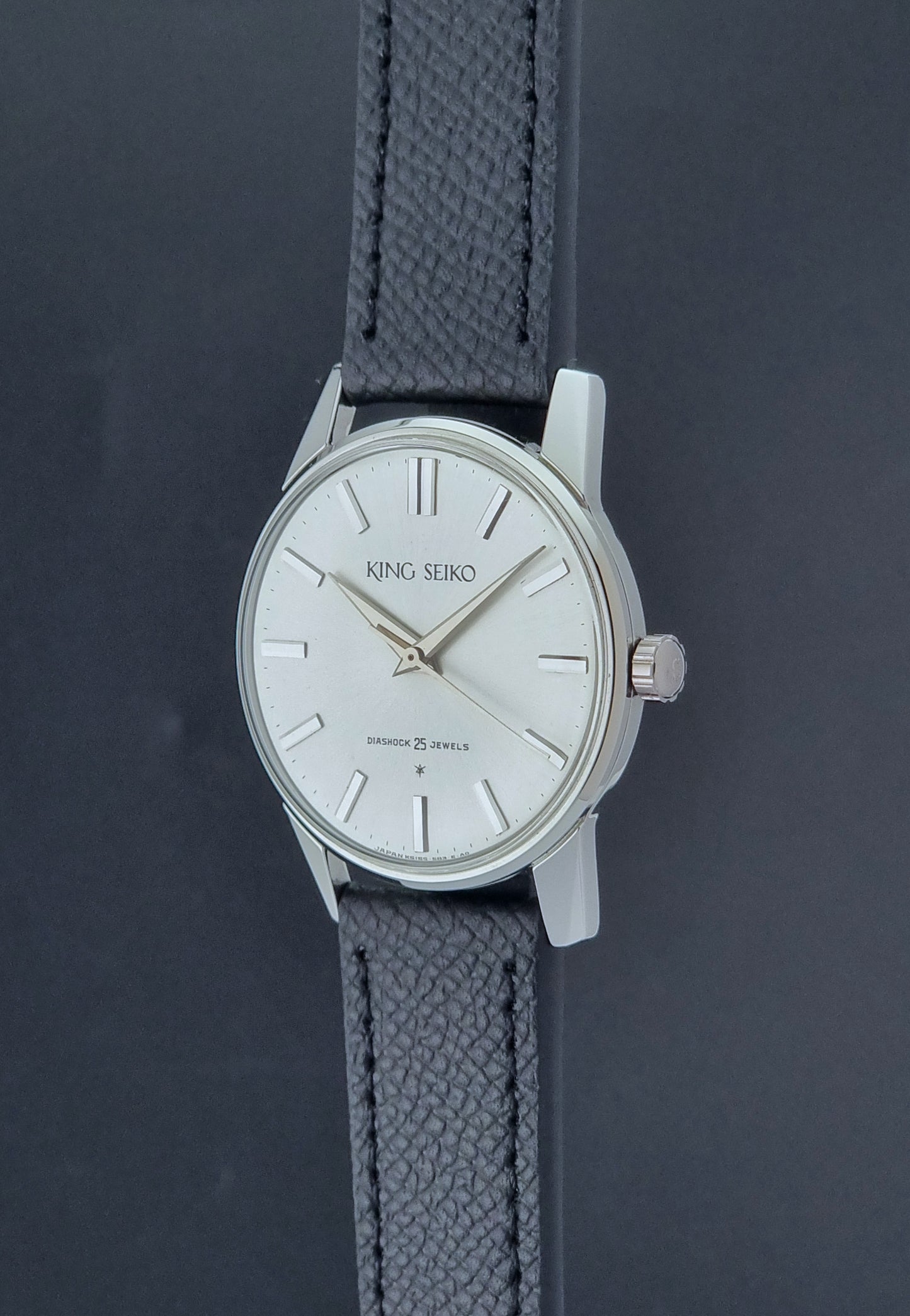 Vintage King Seiko Wristwatch 15034 with a black leather strap on a gray surface crown profile view