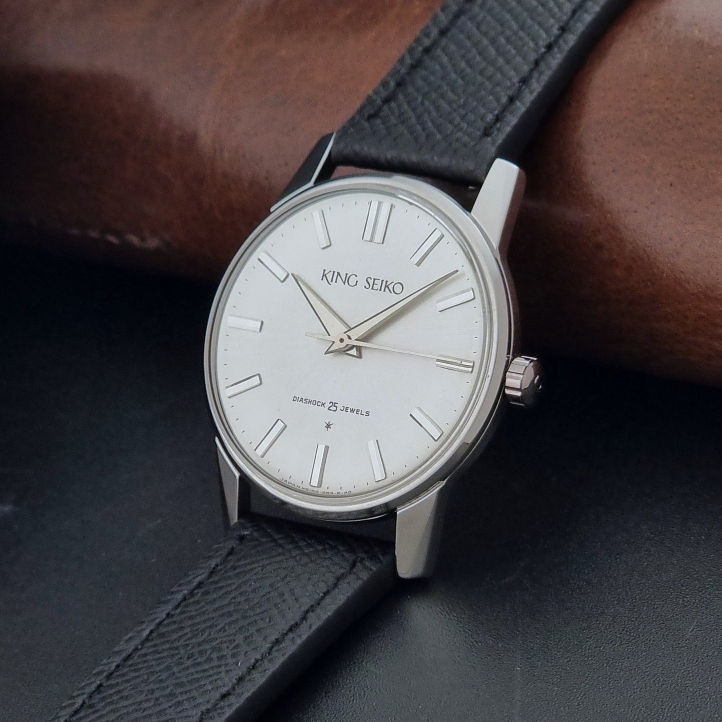 Vintage King Seiko Wristwatch 15034 with a black leather strap on a gray surface crown view
