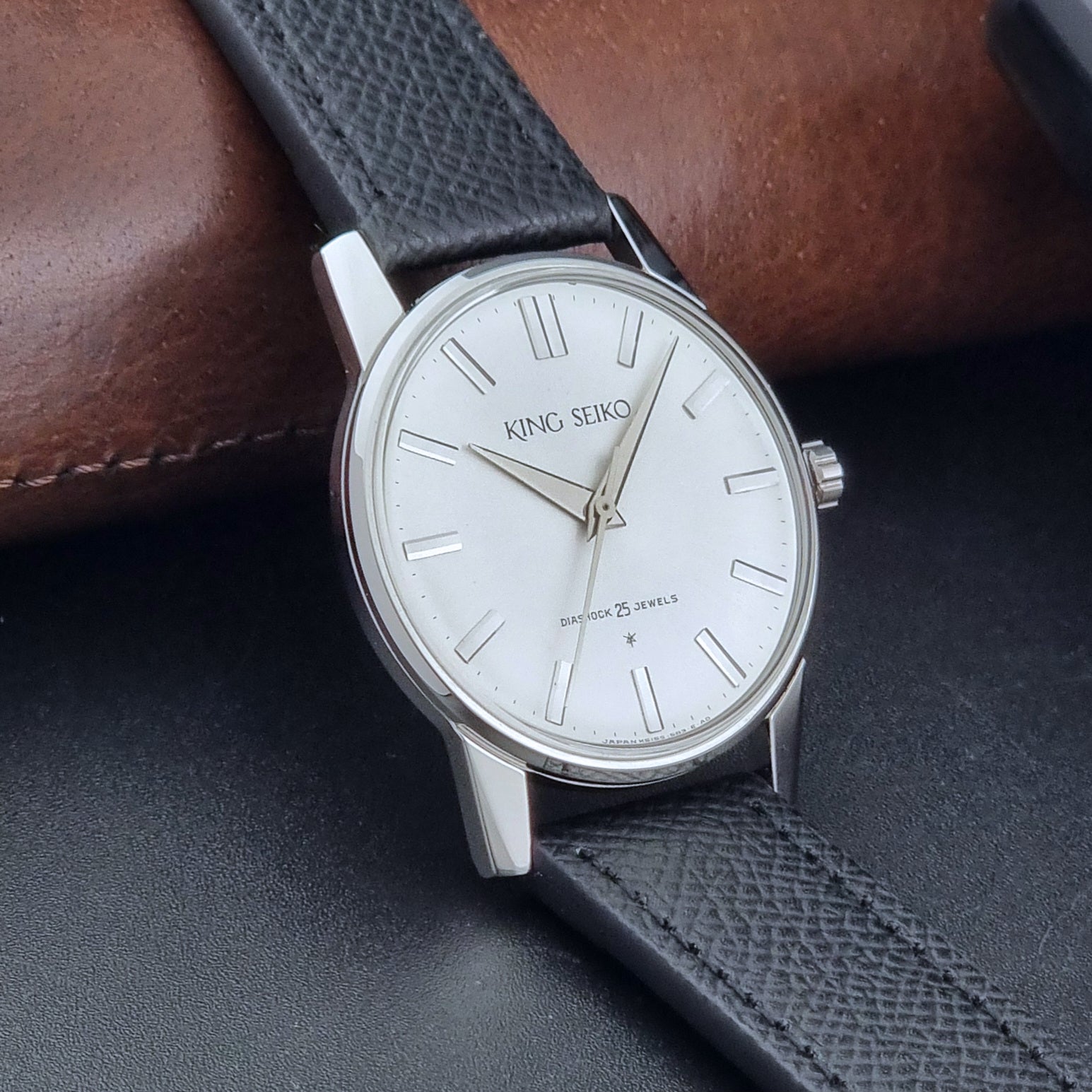 Vintage King Seiko Wristwatch 15034 with a black leather strap on a gray surface side view