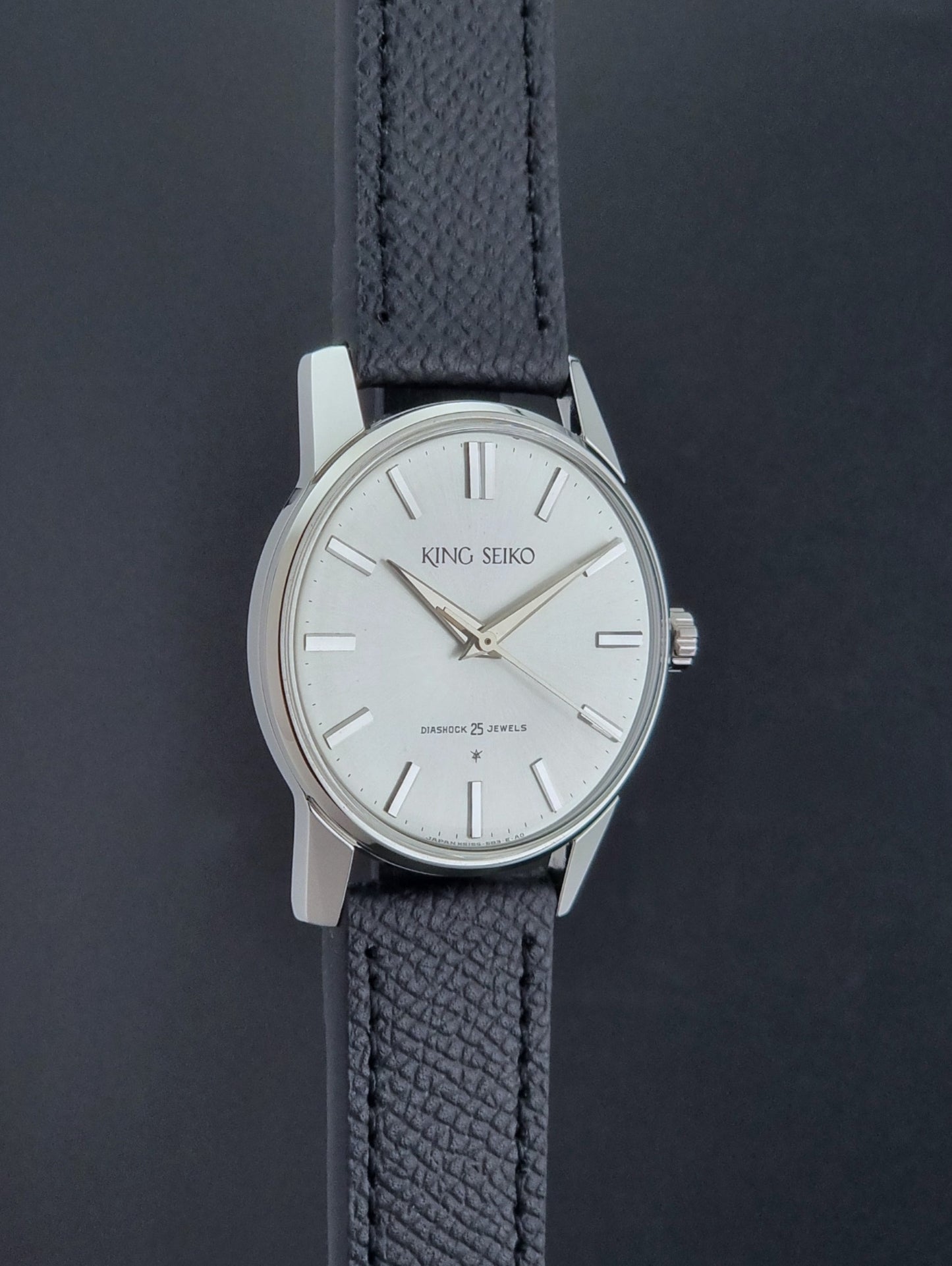 Vintage King Seiko Wristwatch 15034 with a black leather strap on a gray surface side profile view