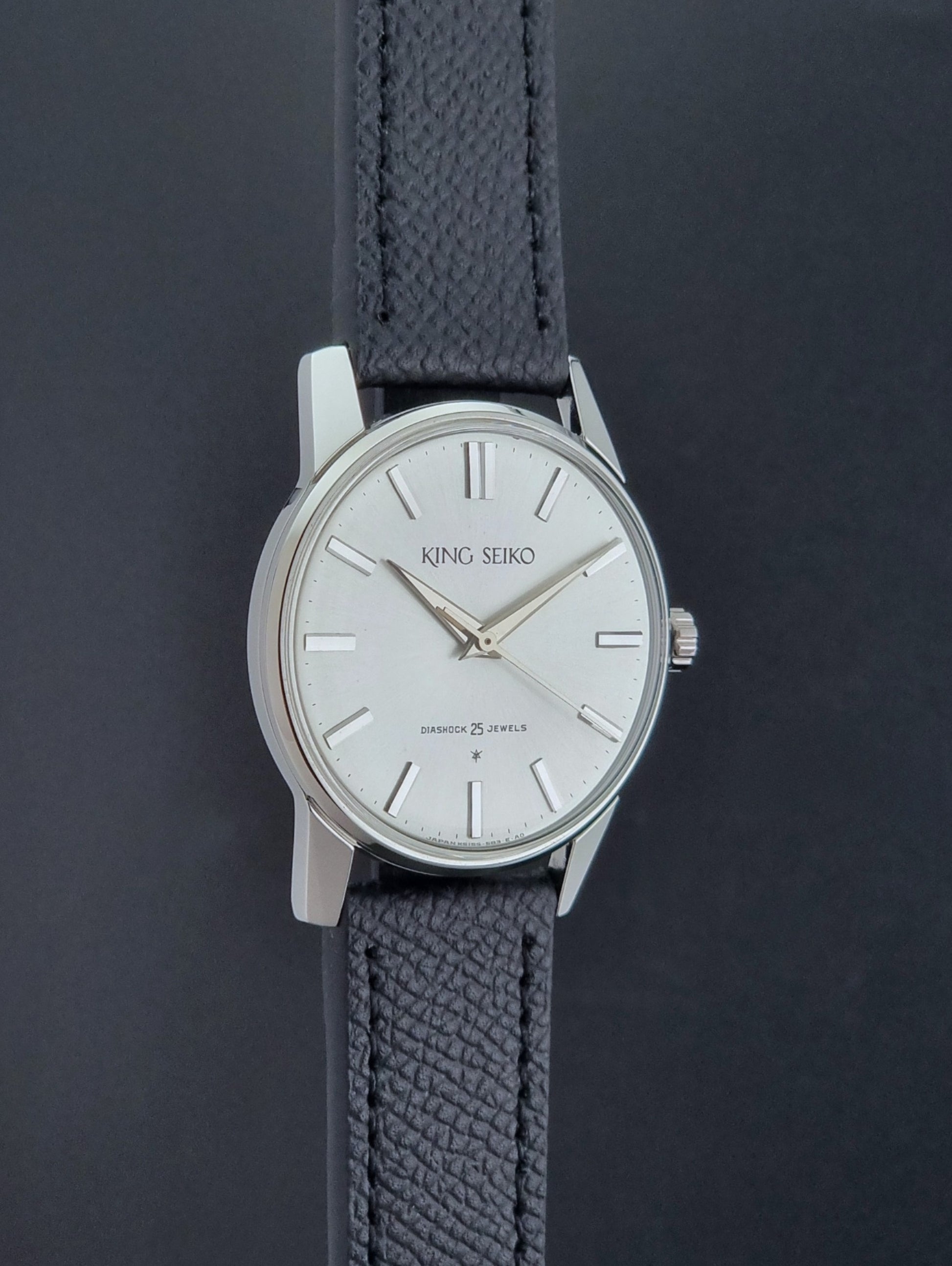 Vintage King Seiko Wristwatch 15034 with a black leather strap on a gray surface side profile view