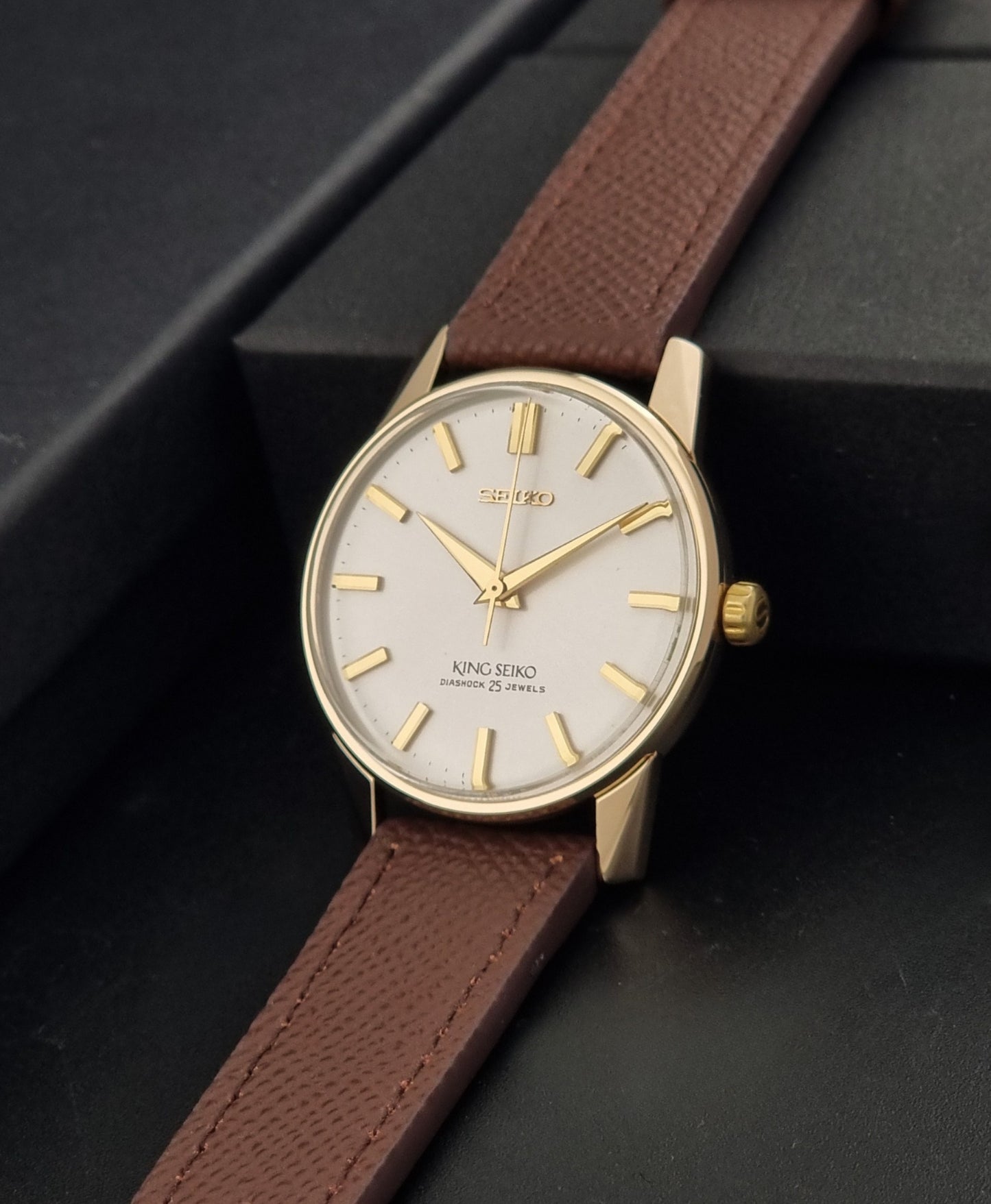 Vintage King Seiko Wristwatch 44-2000 with a gold filled case and brown leather strap on a dark background crown view