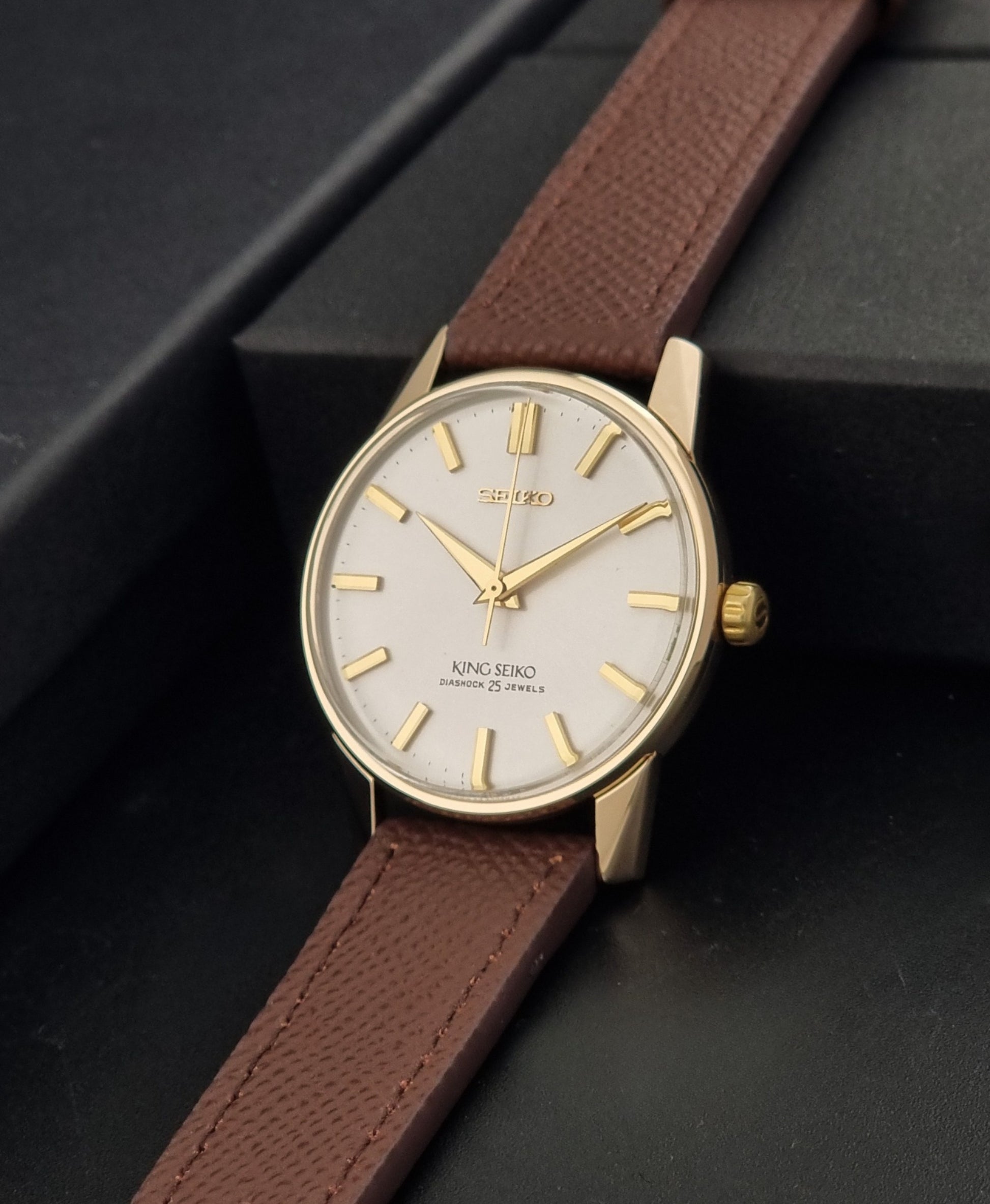 Vintage King Seiko Wristwatch 44-2000 with a gold filled case and brown leather strap on a dark background crown view