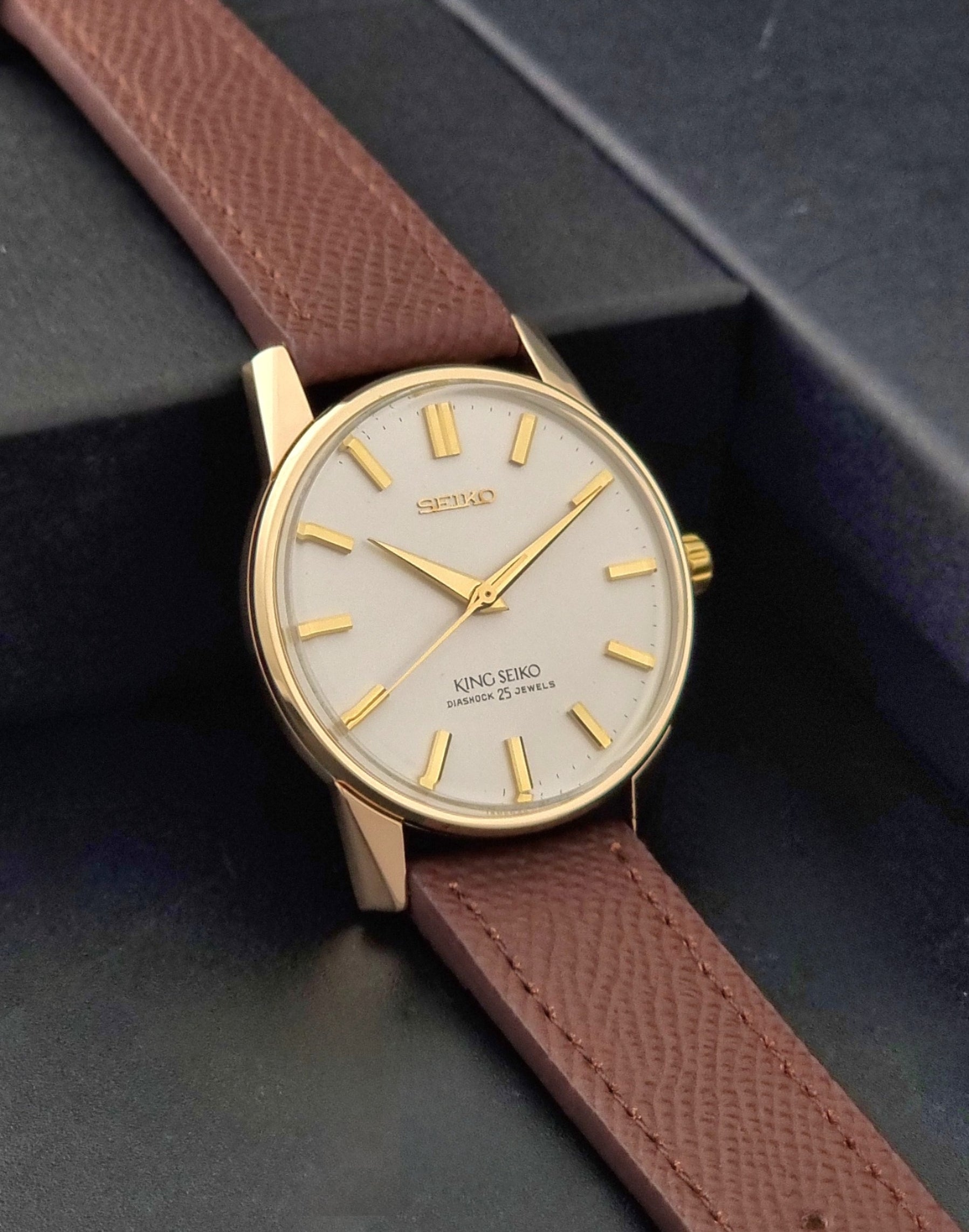 Vintage King Seiko Wristwatch 44-2000 with a gold filled case and brown leather strap on a dark background side view