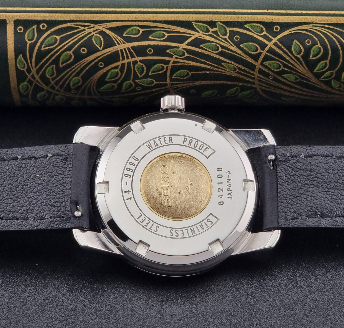 Vintage King Seiko 44-9990 wristwatch with black leather strap and silver case on a dark background case back view