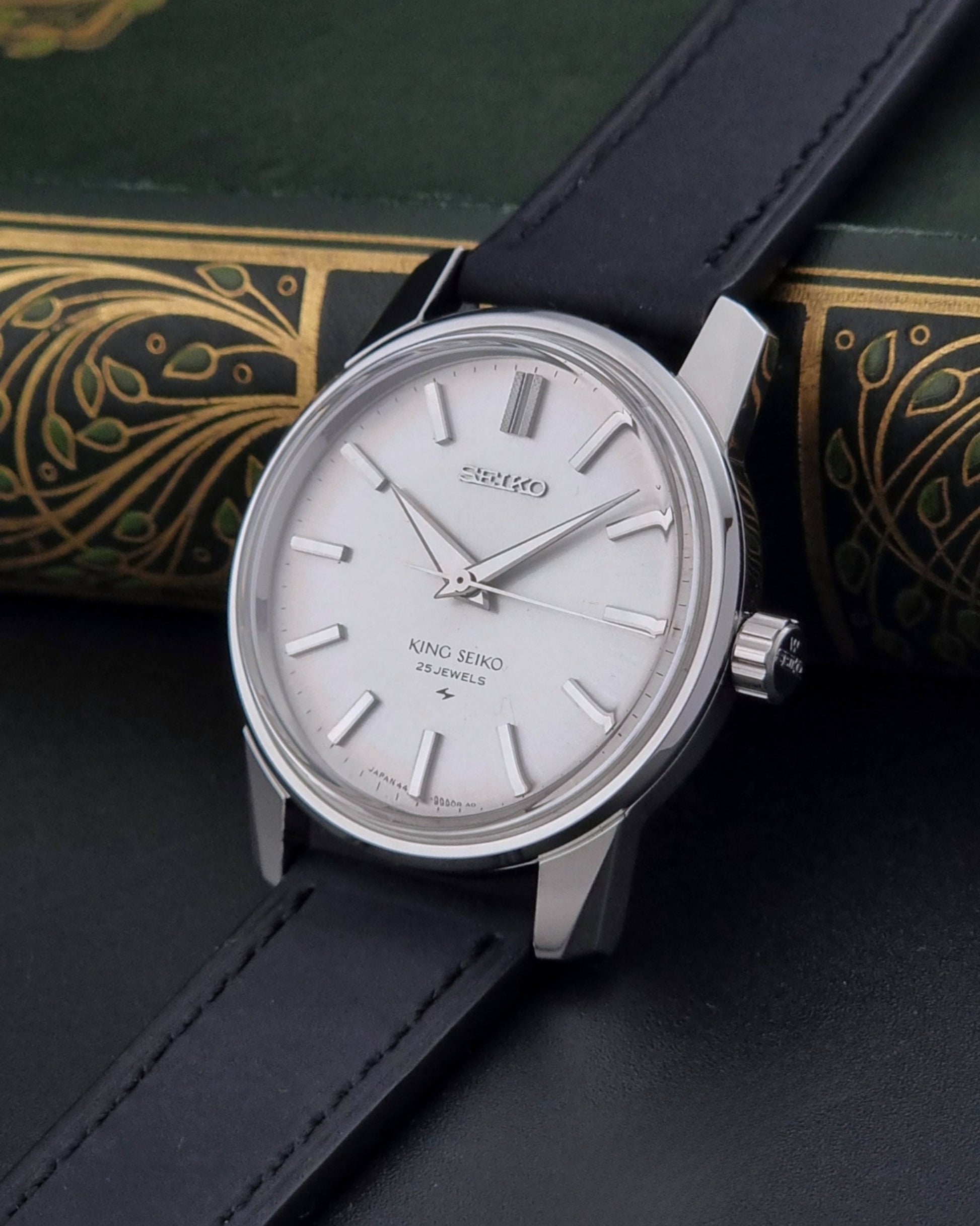 Vintage King Seiko 44-9990 wristwatch with black leather strap and silver case on a dark background crown view