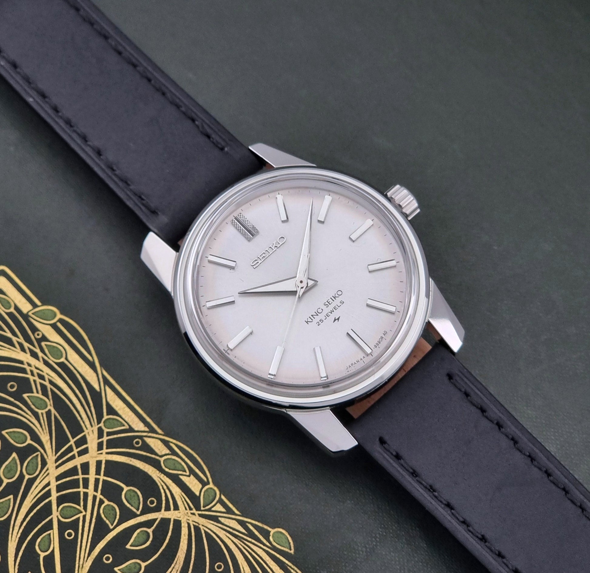 Vintage King Seiko 44-9990 wristwatch with black leather strap and silver case on a dark background front