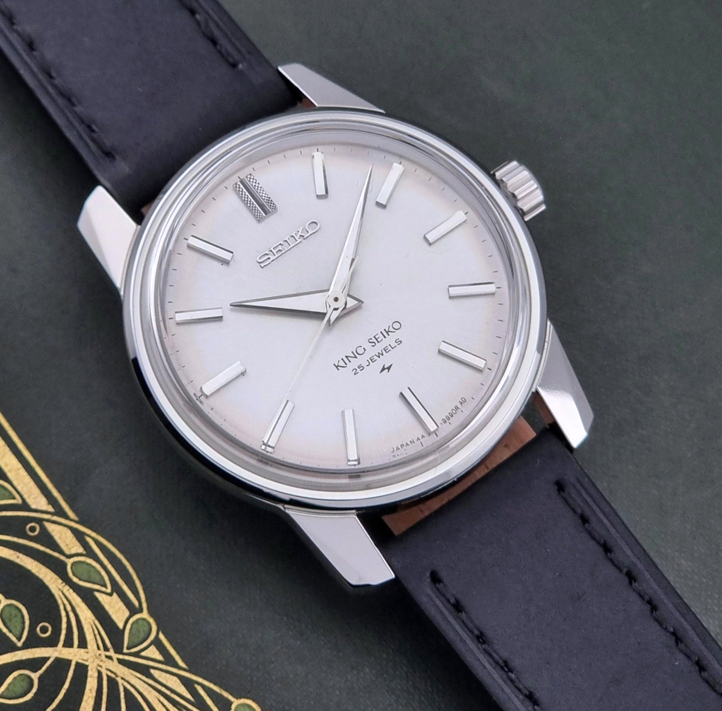Vintage King Seiko 44-9990 wristwatch with black leather strap and silver case on a dark background dial view