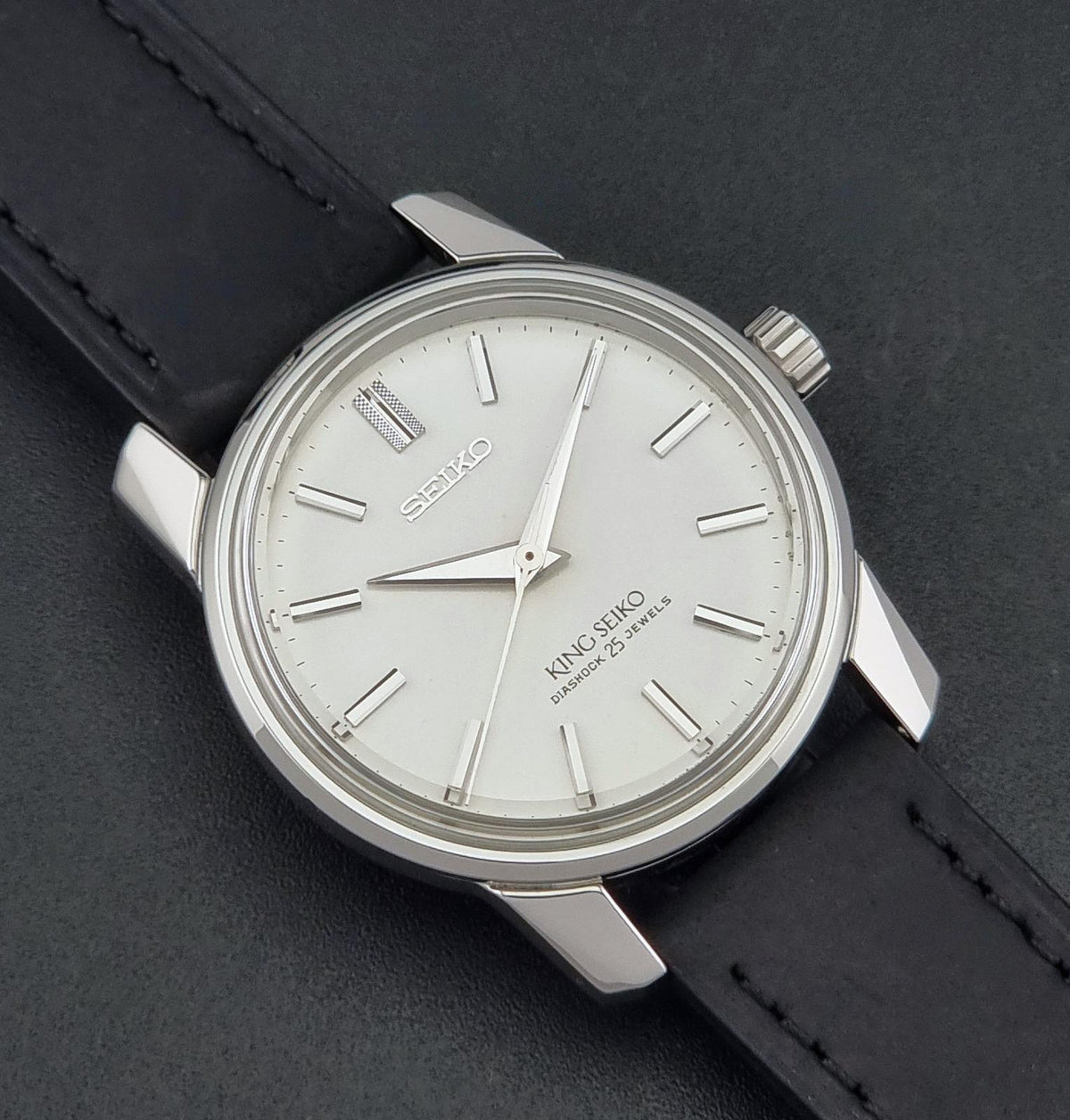 Vintage King Seiko watch 44-9990 with a silver-toned metal case, white dial, and black leather strap, shown on a dark textured background.
