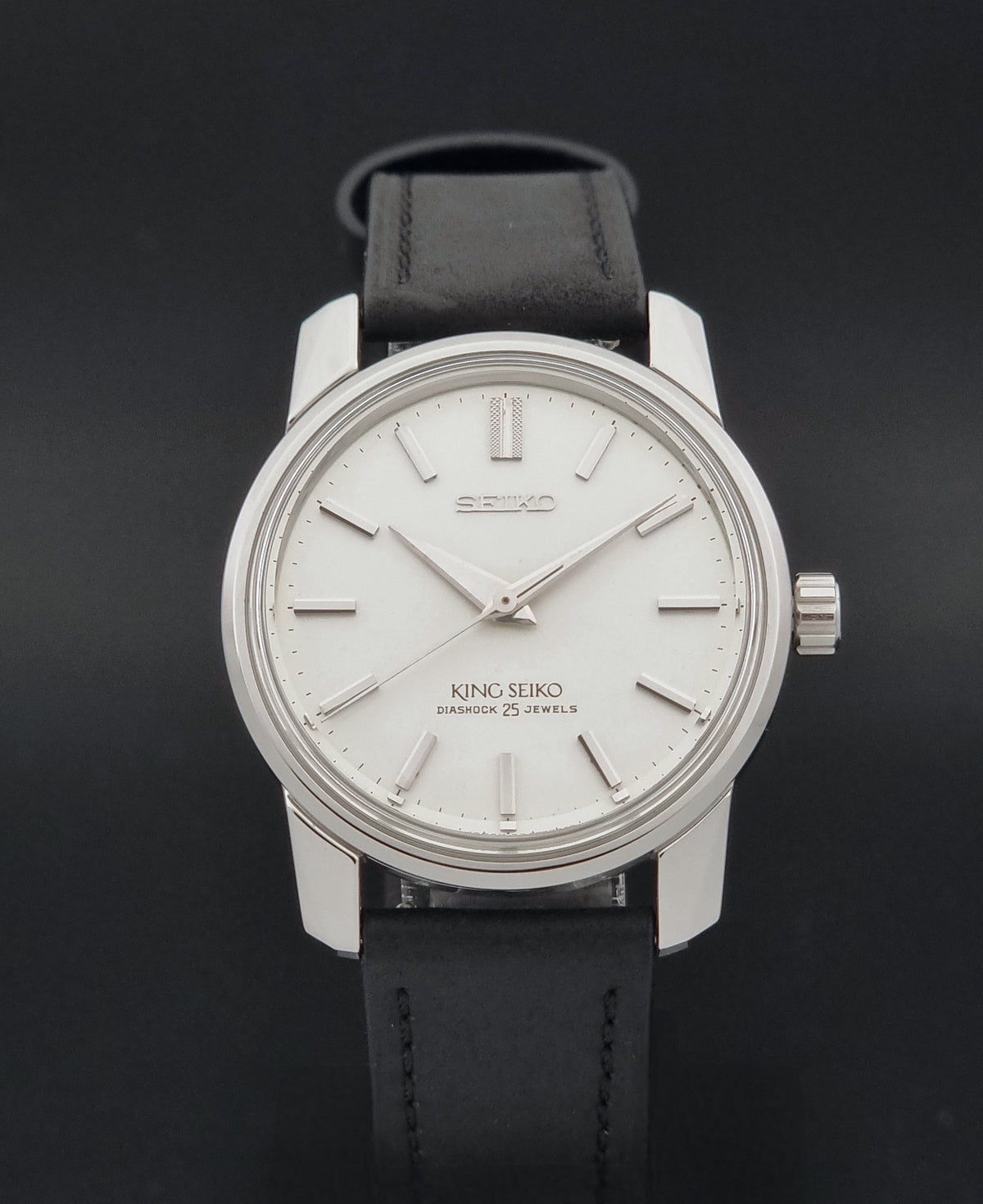Vintage King Seiko watch 44-9990 with a silver-toned stainless steel case, white dial, and black leather strap, shown against a dark background.