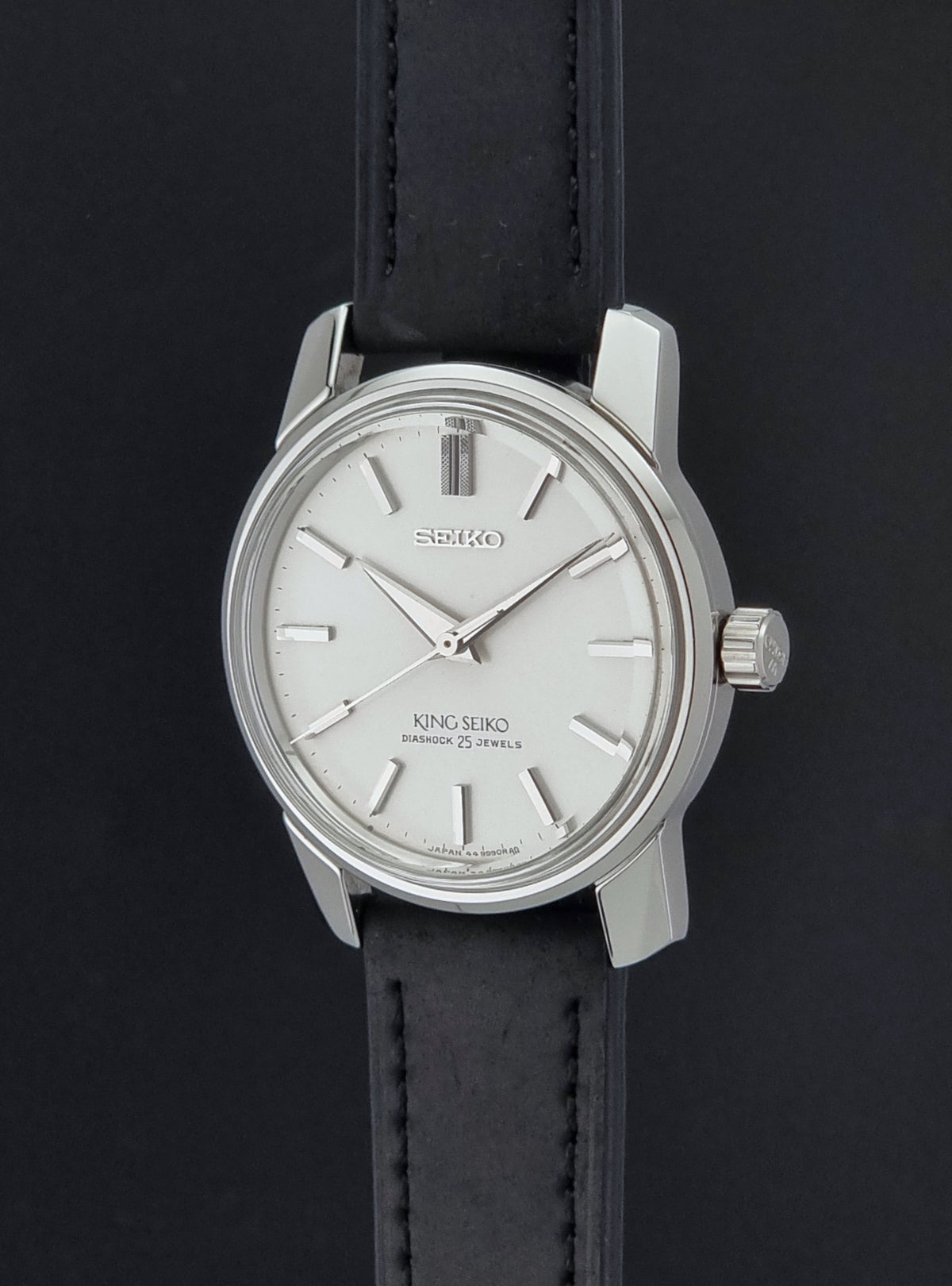 Vintage King Seiko watch 44-9990 with a silver-toned metal case, white dial, and black leather strap, photographed against a dark background.