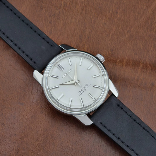 Vintage King Seiko 44-999 Watch with black leather strap and silver case on a brown textured background
