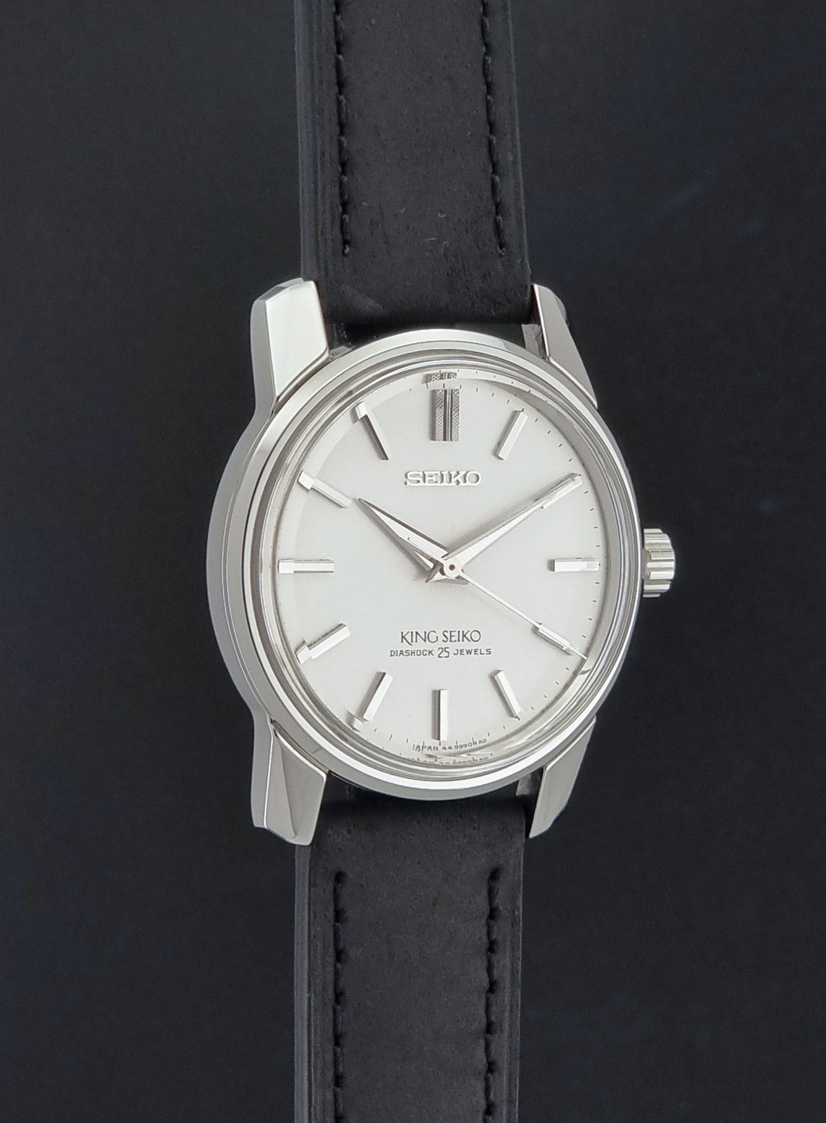 Vintage King Seiko watch 44-9990 with a silver-toned metal case, white dial, and black leather strap, shown against a dark background.