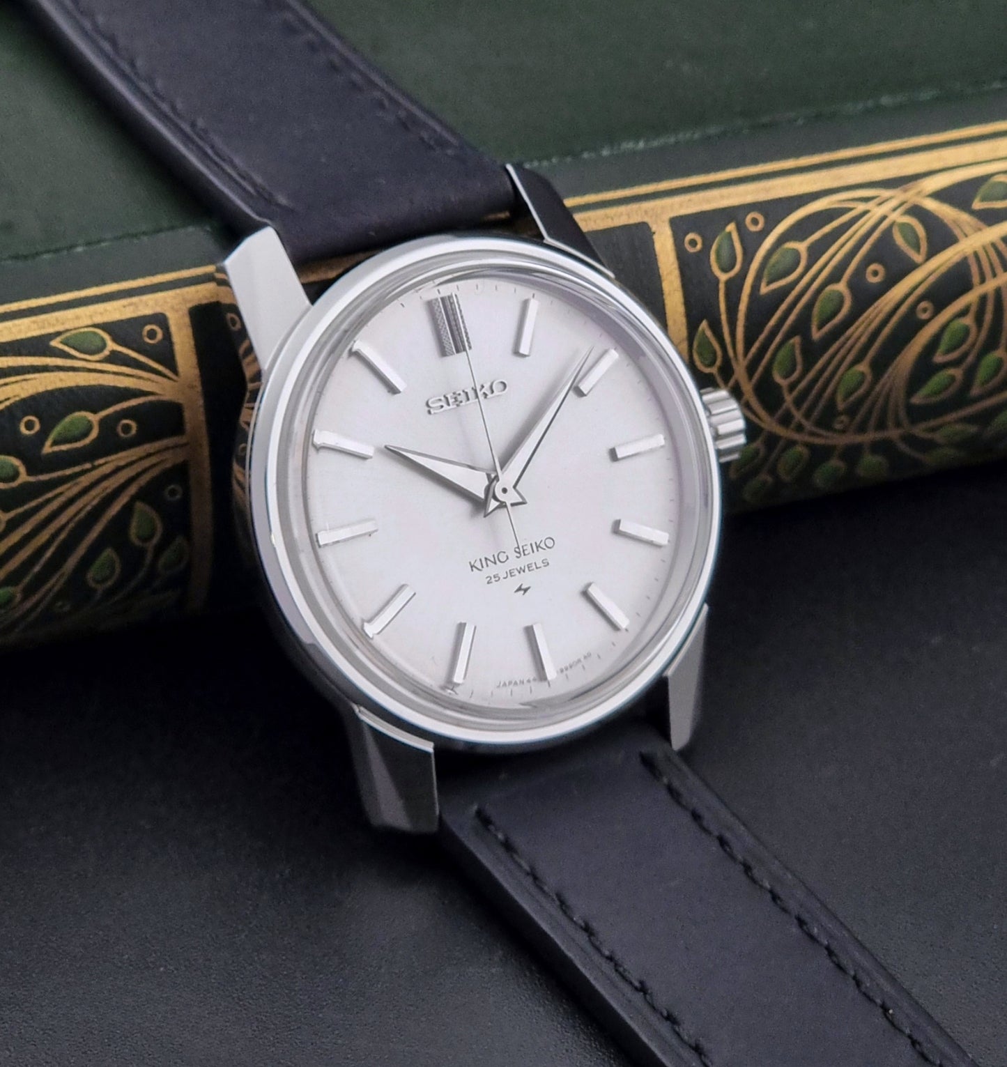 Vintage King Seiko 44-9990 wristwatch with black leather strap and silver case on a dark background side view