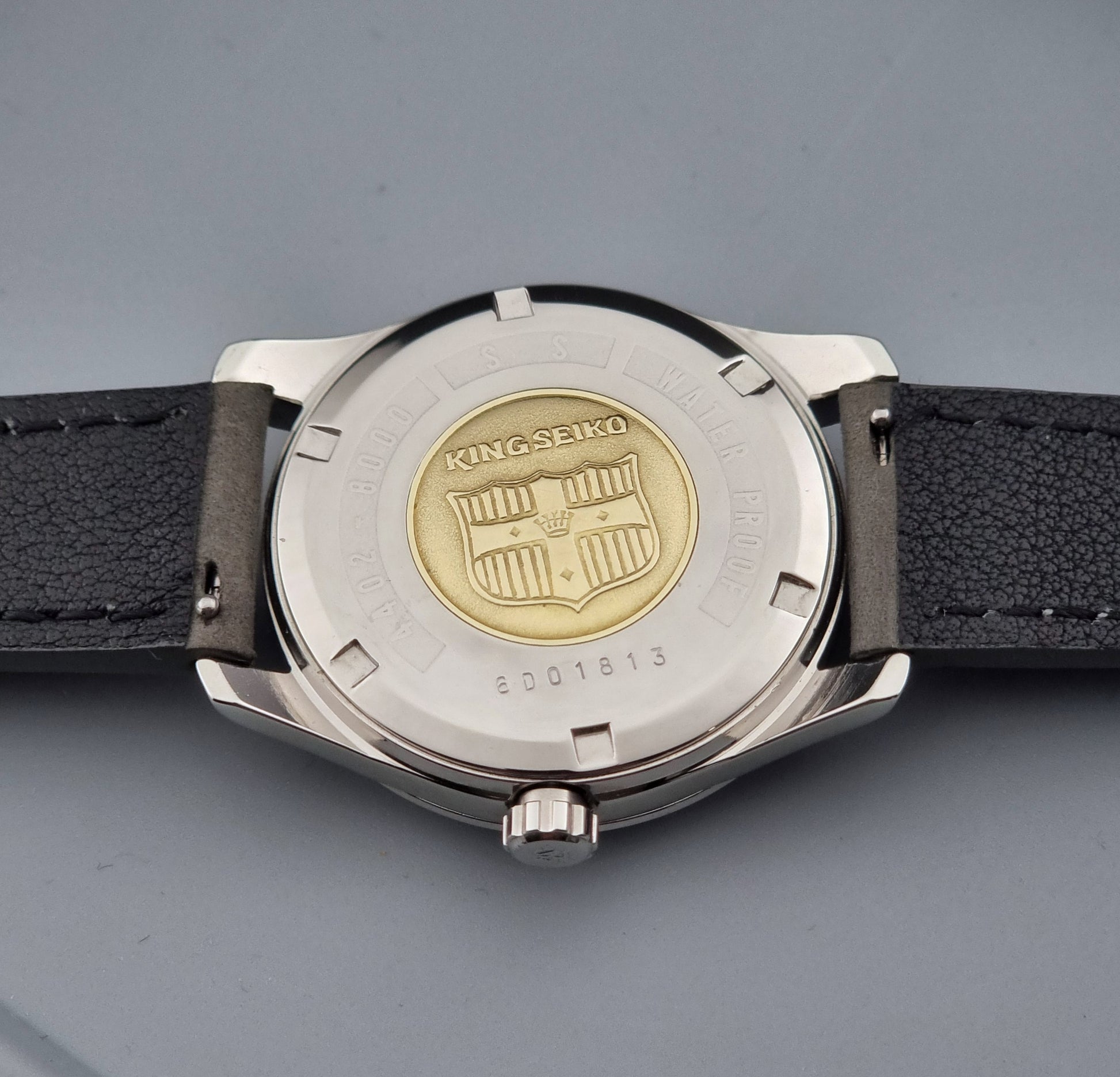 Vintage King Seiko 4402-8000 watch with a silver case and grey leather strap on a gray background case back view