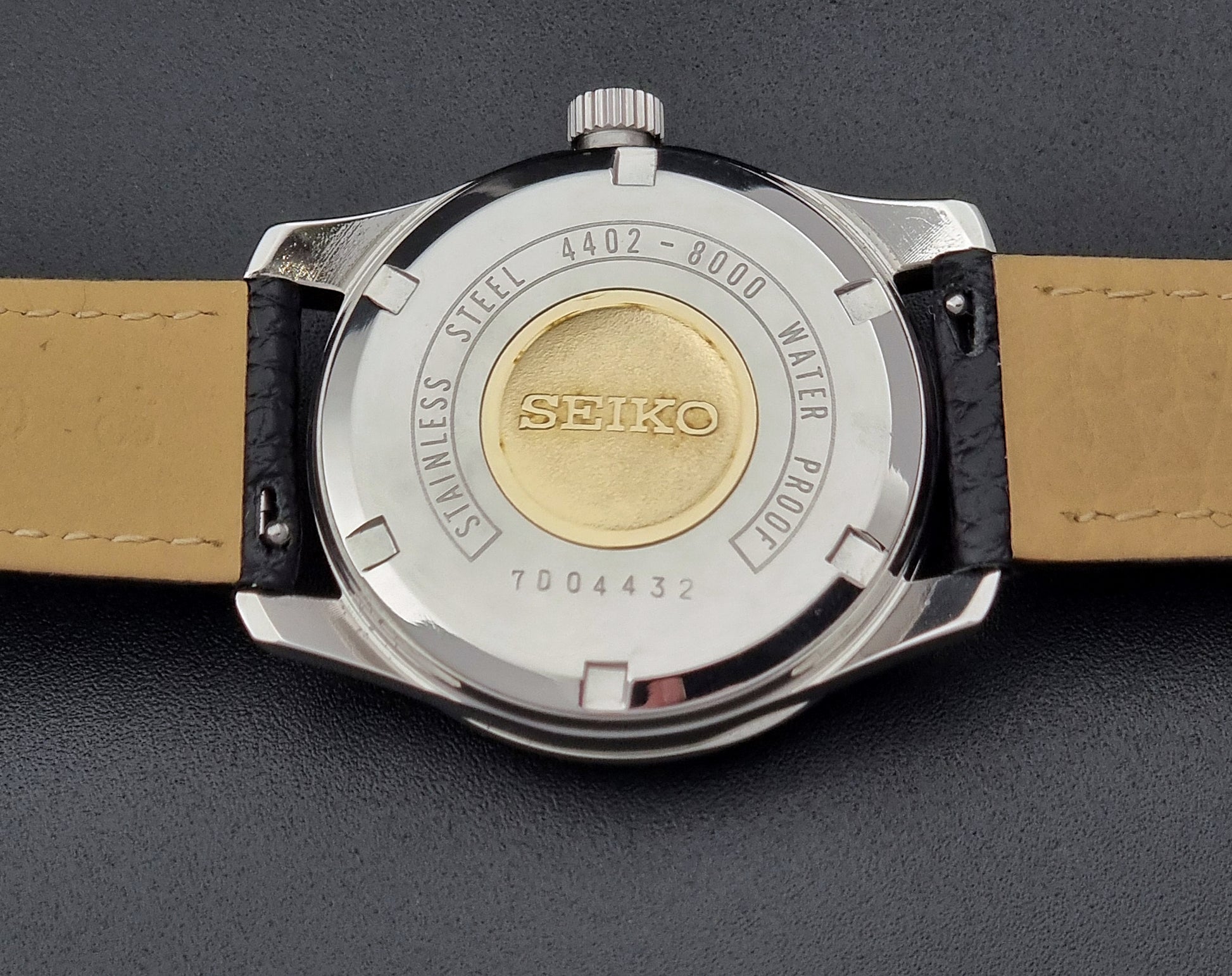 Vintage King Seiko Wristwatch 4402-8000 on a black leather strap on a dark background case back with gold medallion 